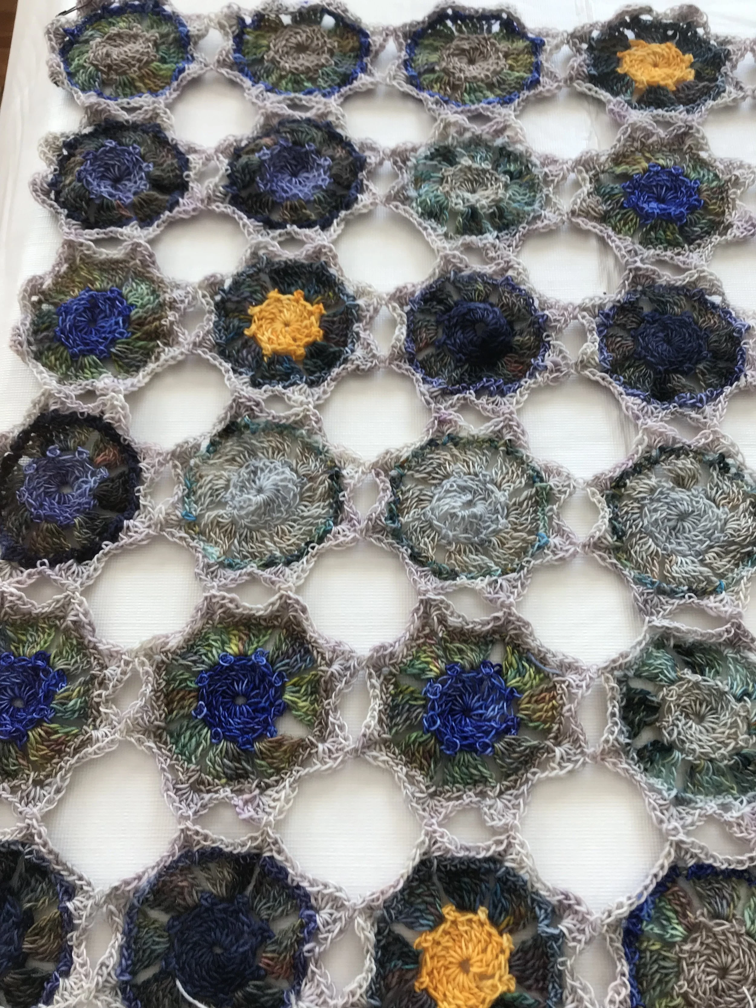 Close-up of a handmade crochet blanket with hexagonal patches featuring colorful floral patterns, connected by a purple yarn border.