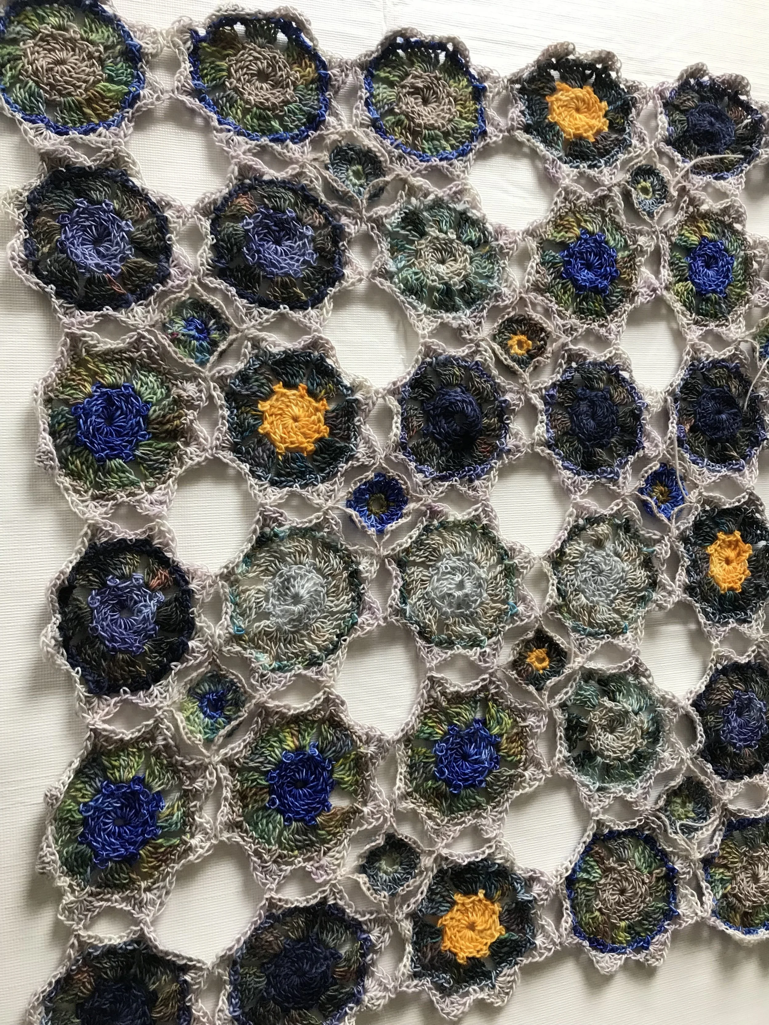 Handmade crochet piece with interconnected circular motifs featuring colorful embroidery, including blue, green, yellow, and black thread on a light background.