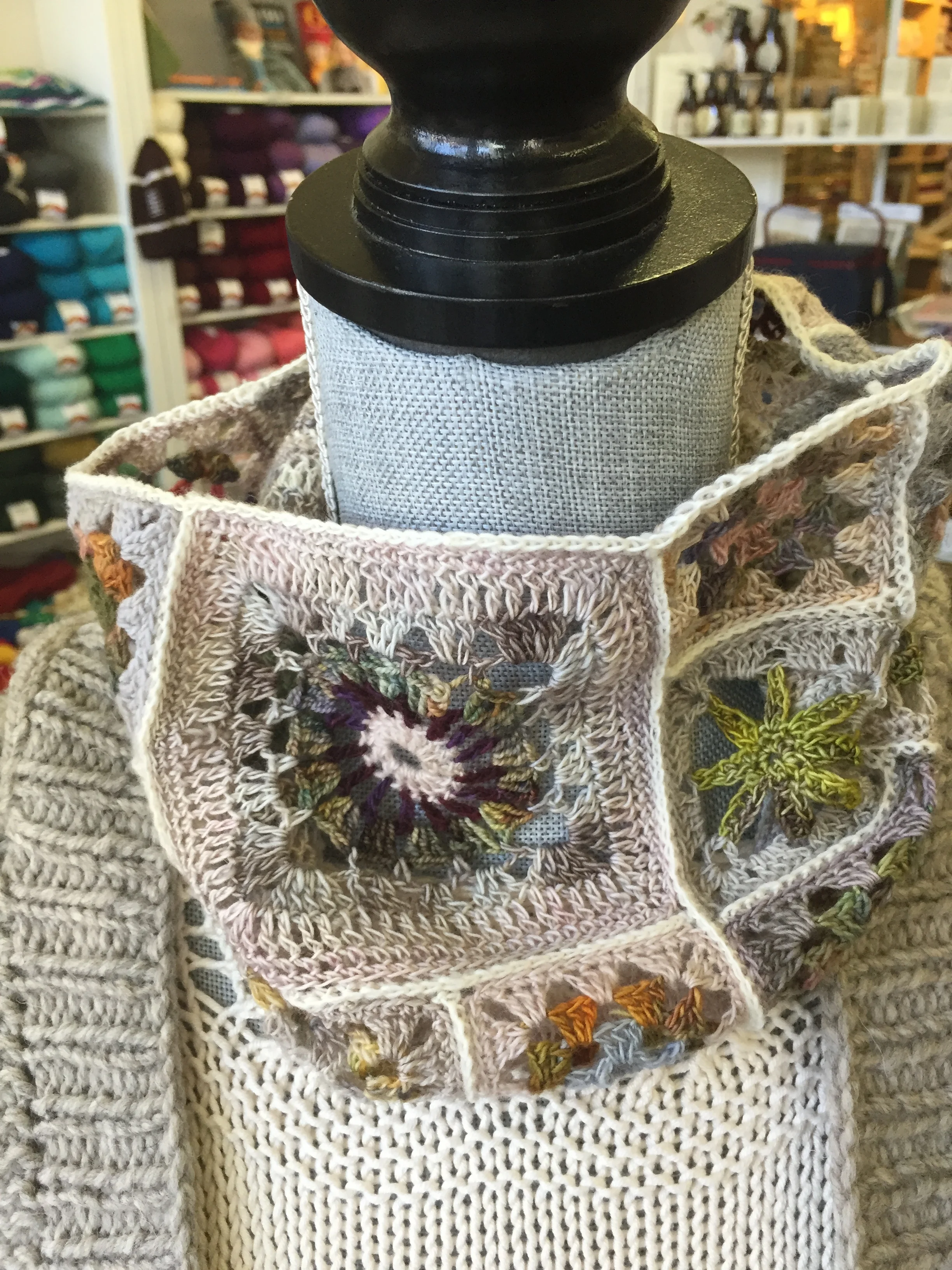 Display of crochet or knitted accessories with floral and star designs on a mannequin display in a craft store.