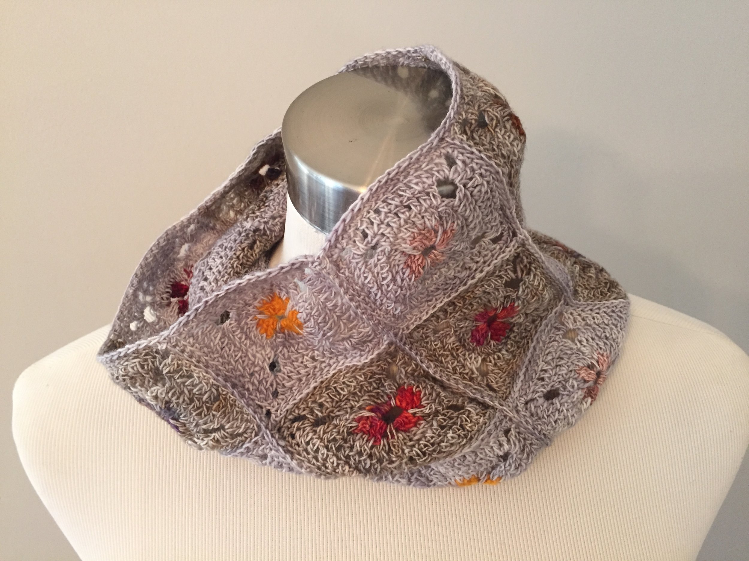 Hand-knit scarf with embroidered orange, red, and black flowers, wrapped around a mannequin neck.