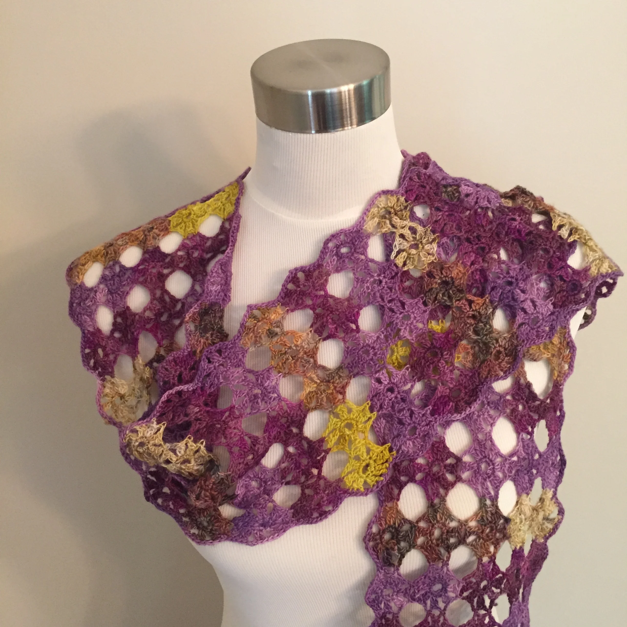 Colorful crocheted shawl draped over a white mannequin with a metallic neck cap.