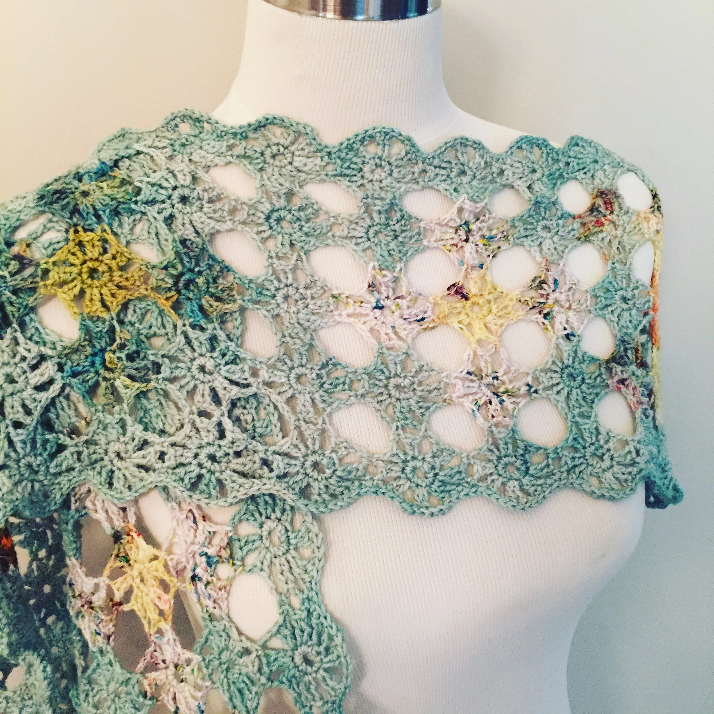 A mannequin wearing a multicolored crocheted shawl with open spaces and intricate pattern.