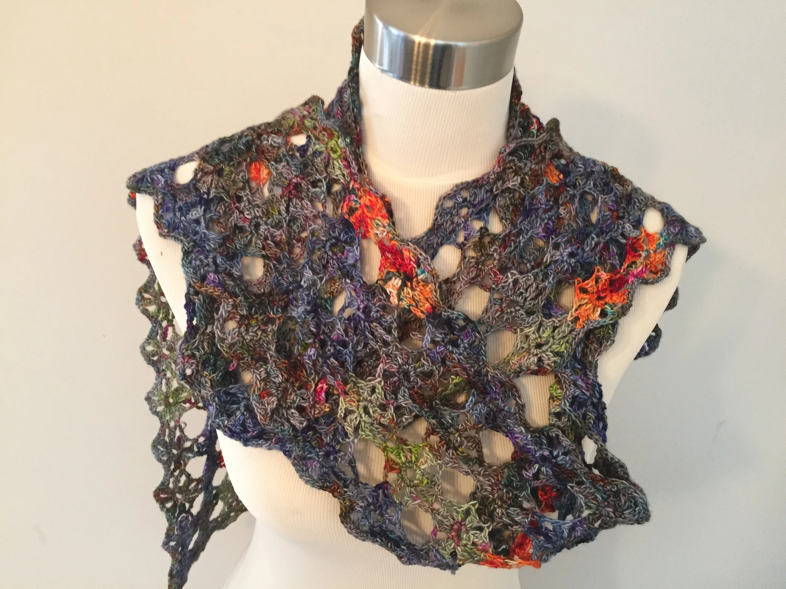 Colorful, open-knit crochet scarf displayed on a white mannequin with a silver neck.