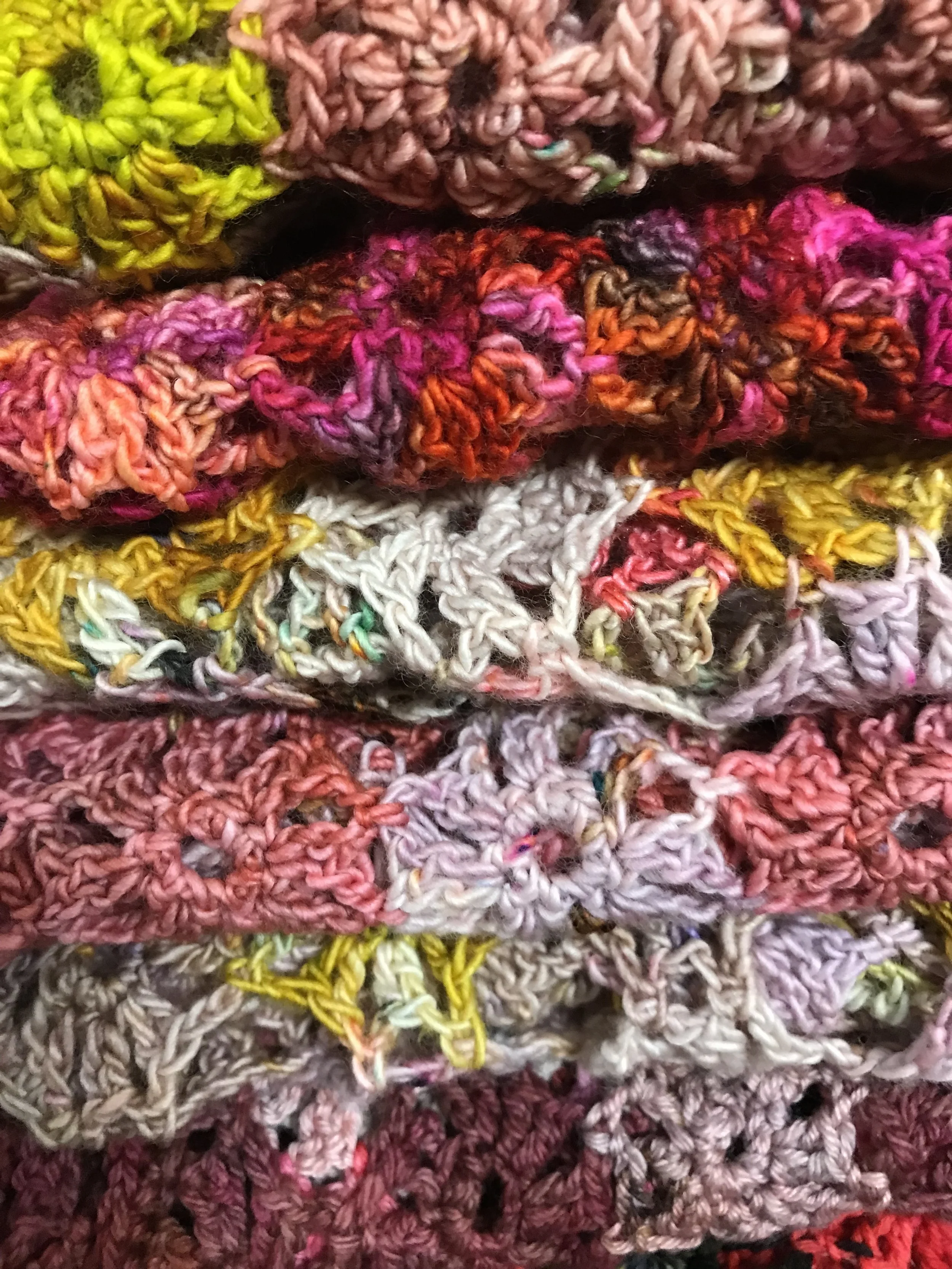 Close-up photo of colorful, overlapping yarn or crochet items in various colors and textures.