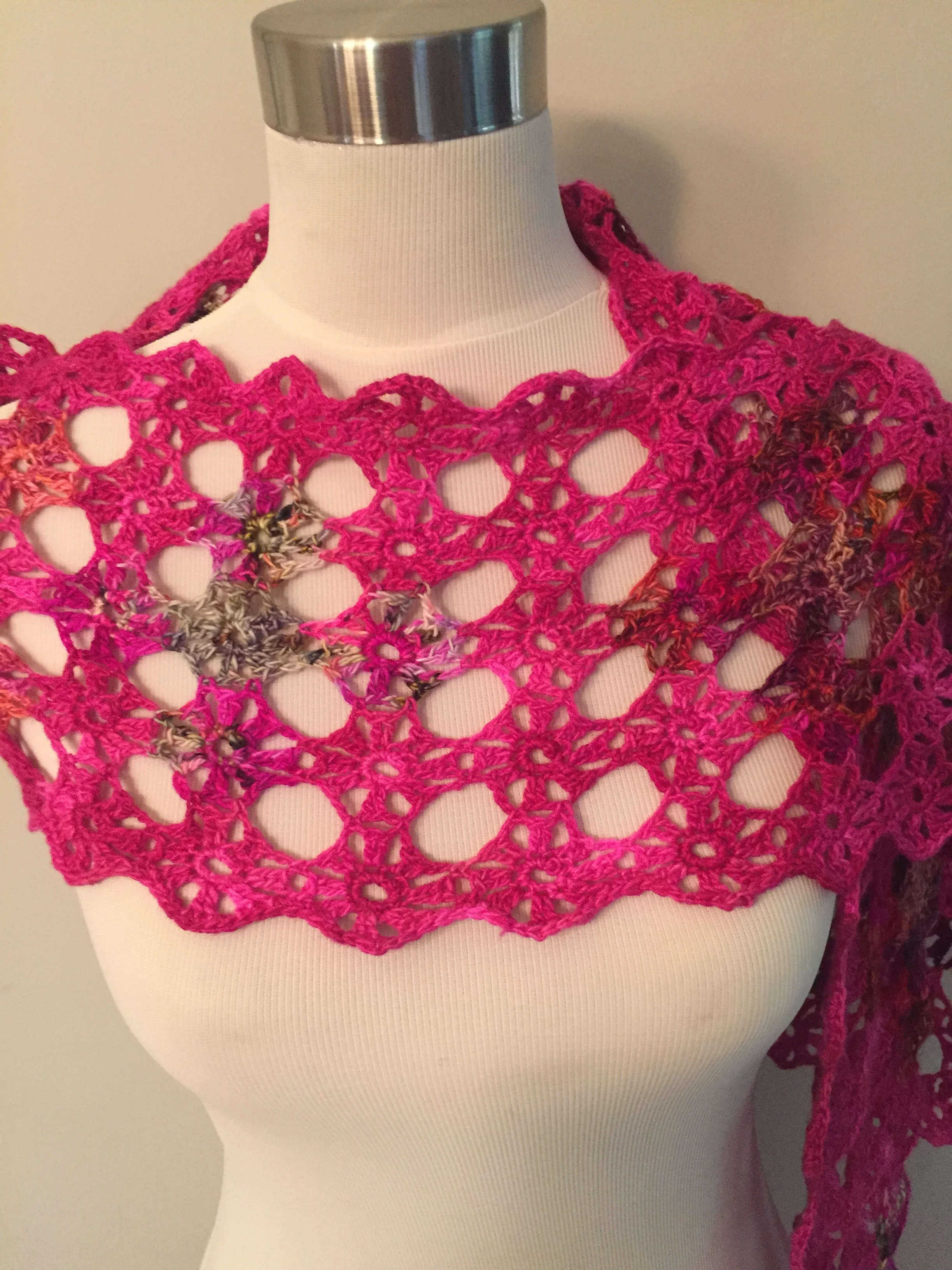 Pink crochet shawl with floral accents on a mannequin.
