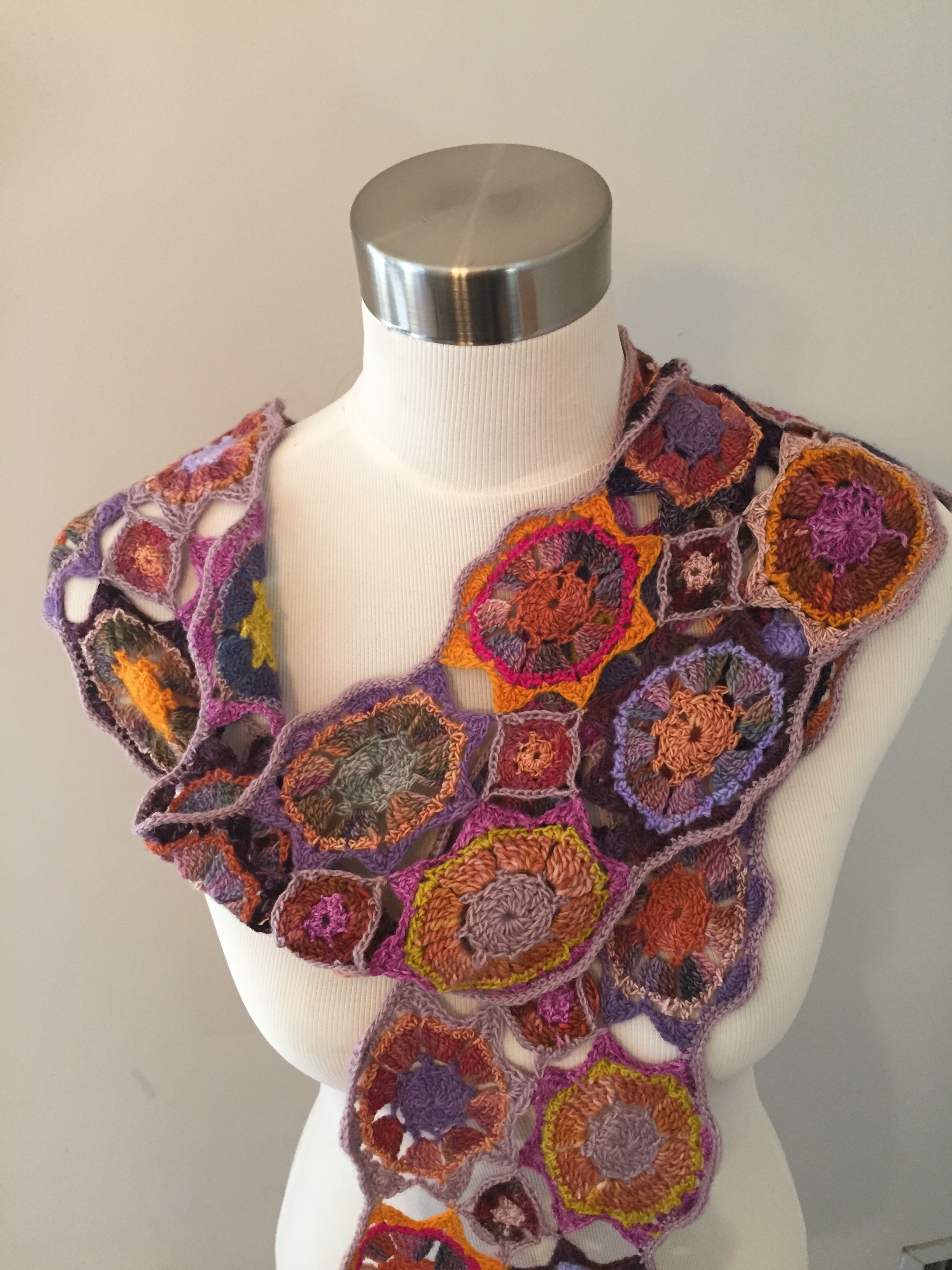 A white mannequin torso wearing a handmade crochet shawl with colorful, circular patterns.