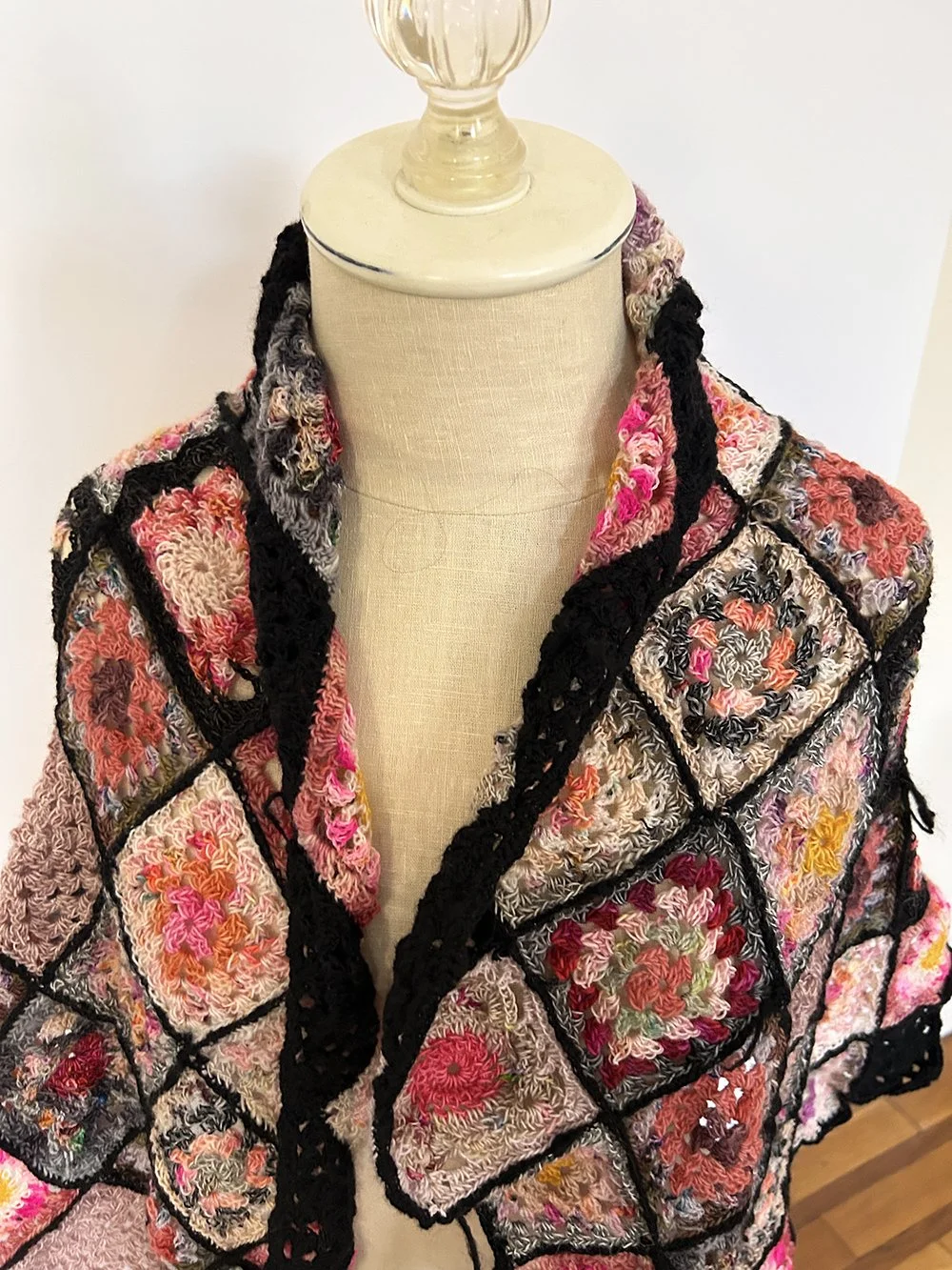 A crochet jacket with colorful floral patterns and black border accents displayed on a mannequin.