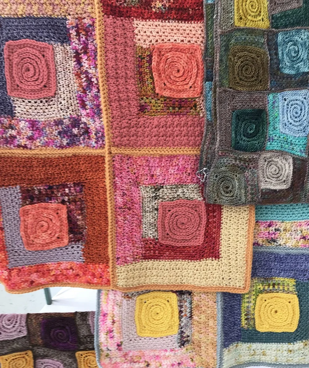 Close-up of colorful, handmade crochet patchwork blankets with various geometric squares and spiral patterns