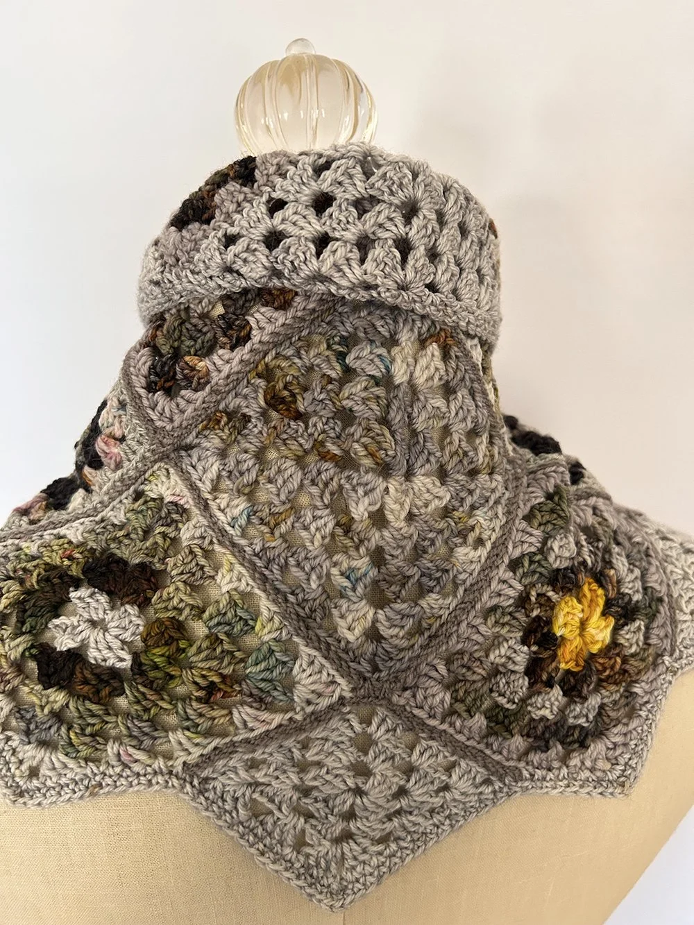 Handmade crocheted multicolored blanket with floral patterns, draped over a mannequin with a glass pumpkin on top.