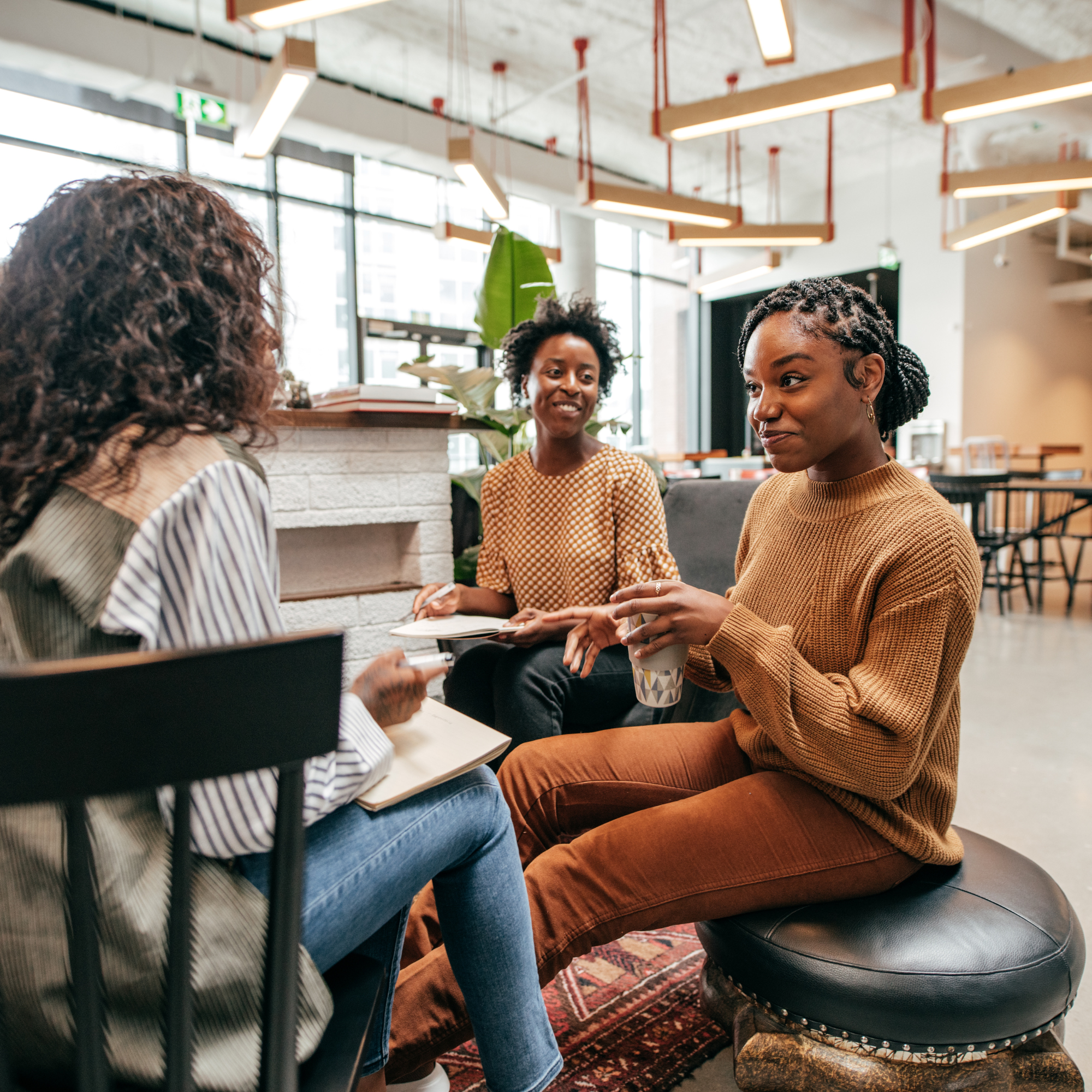 three women sitting in a group at at table having a discussion.