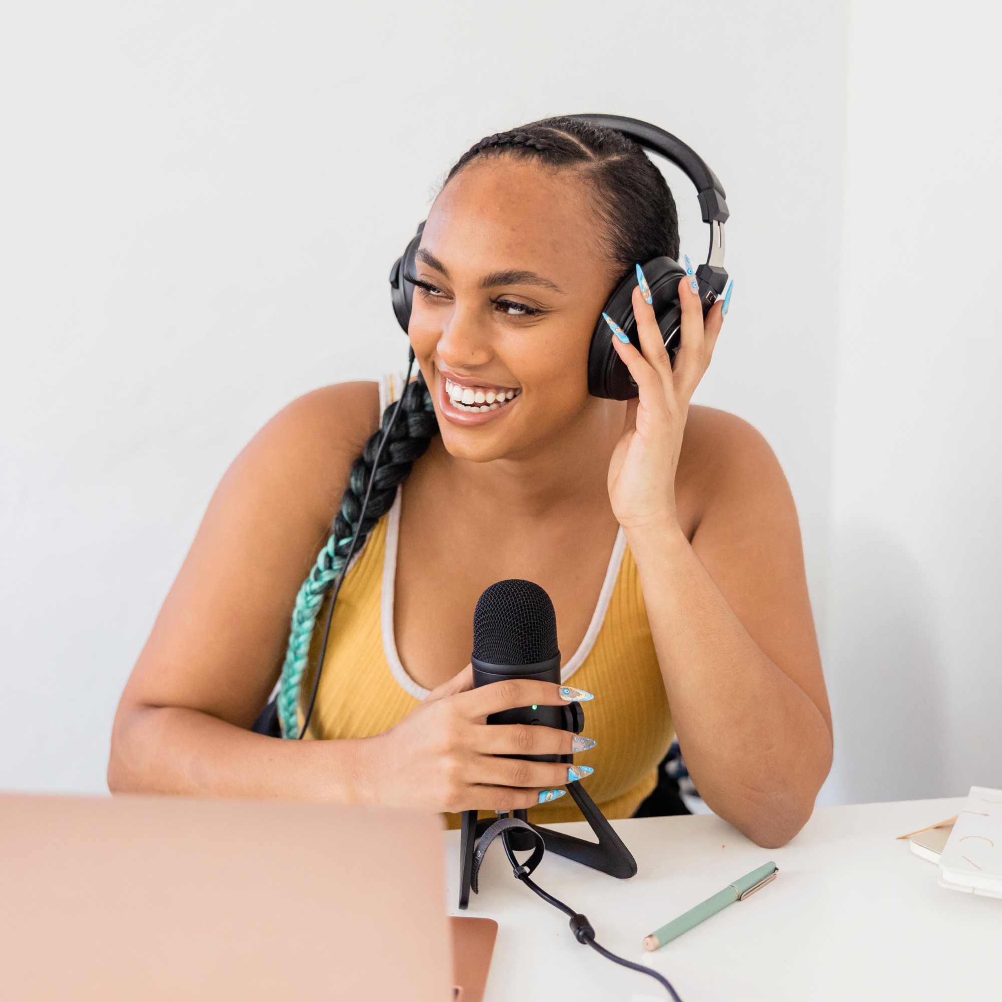 Woman of colour smiling looking out to her right hand side wearing headphones and holding a microphone .