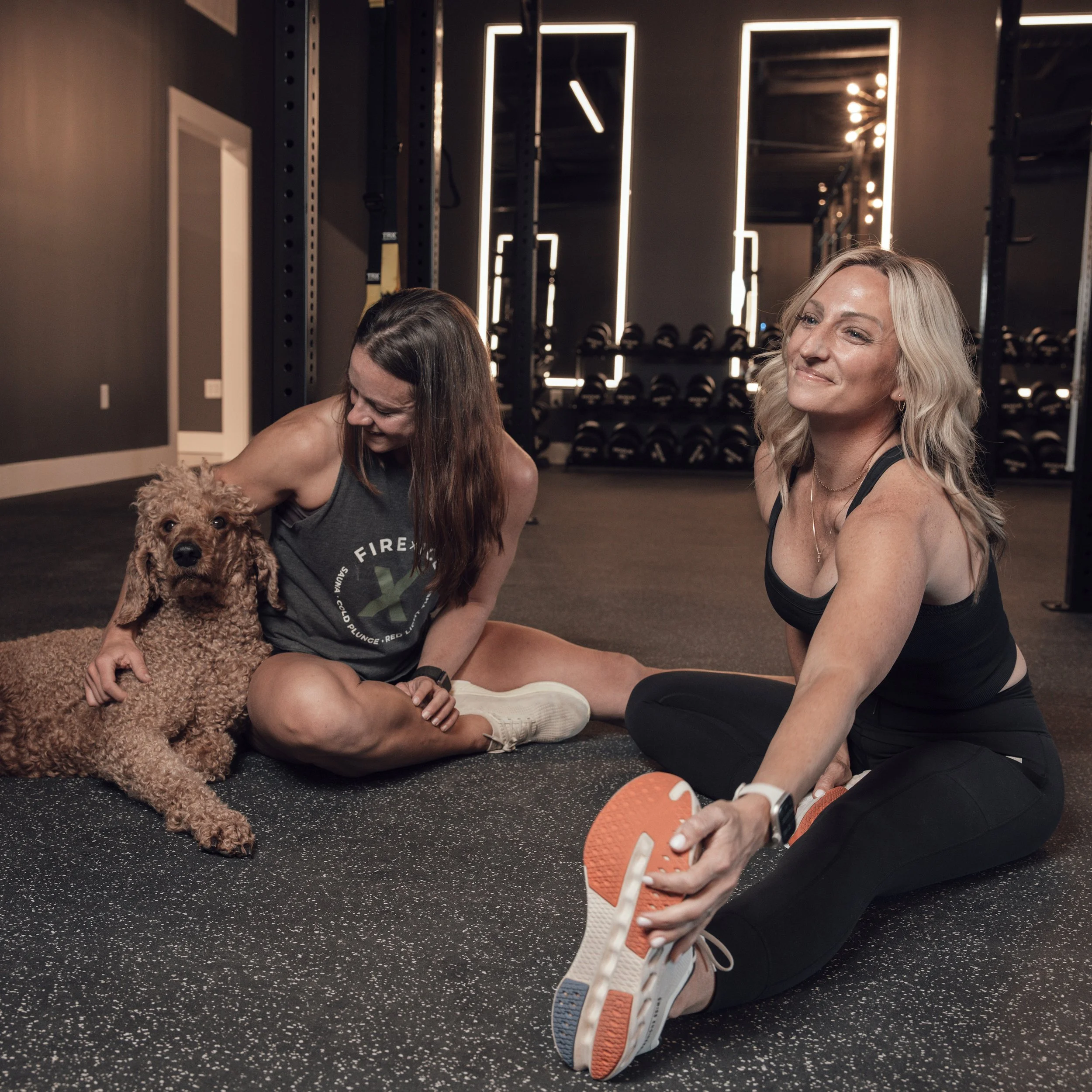 Two women sitting and stretching in a gym