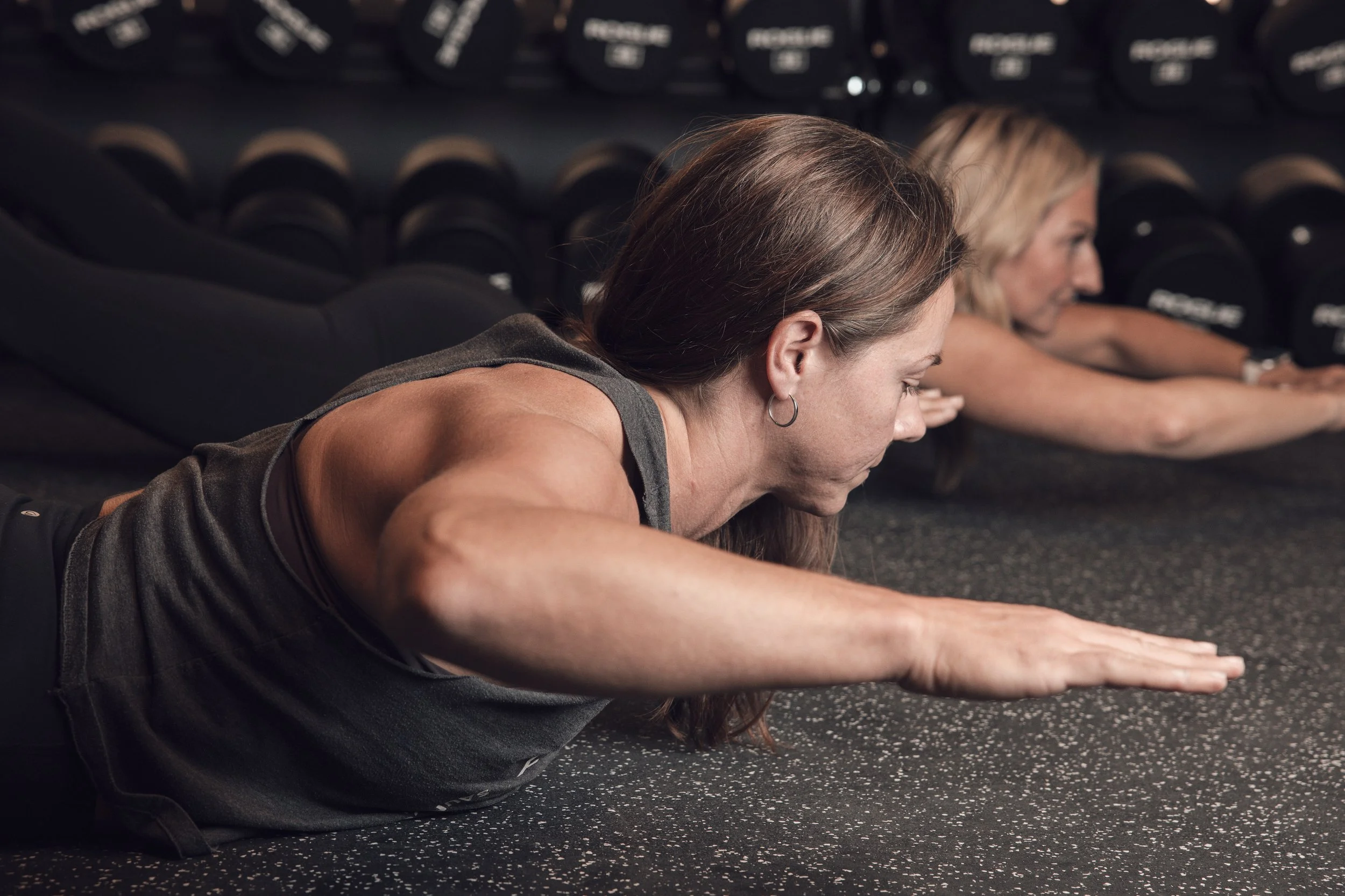 Two women exercising in a gym doing plank pose on the floor