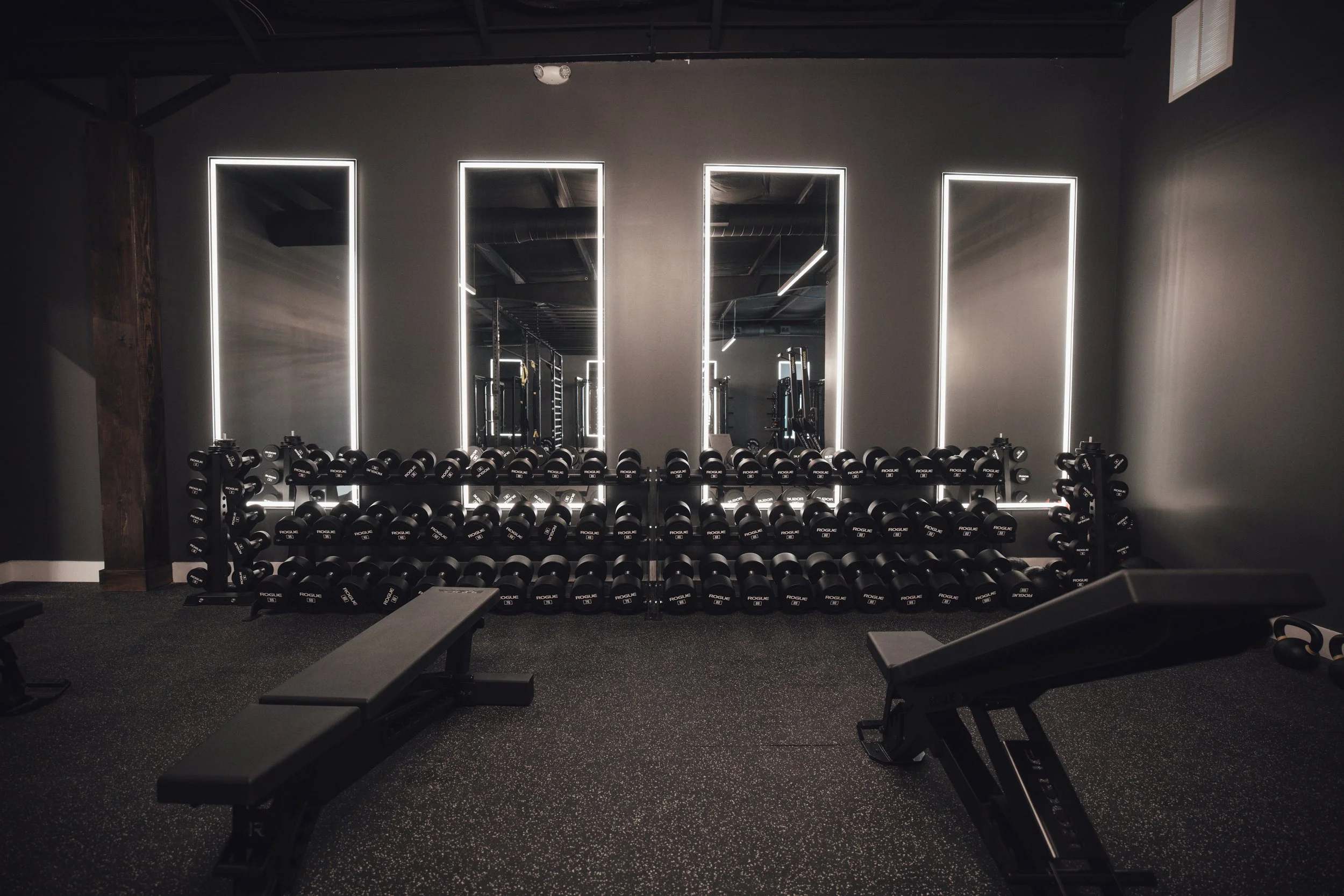 Gym with mirrored wall, illuminated rectangular mirrors, and black dumbbells on racks