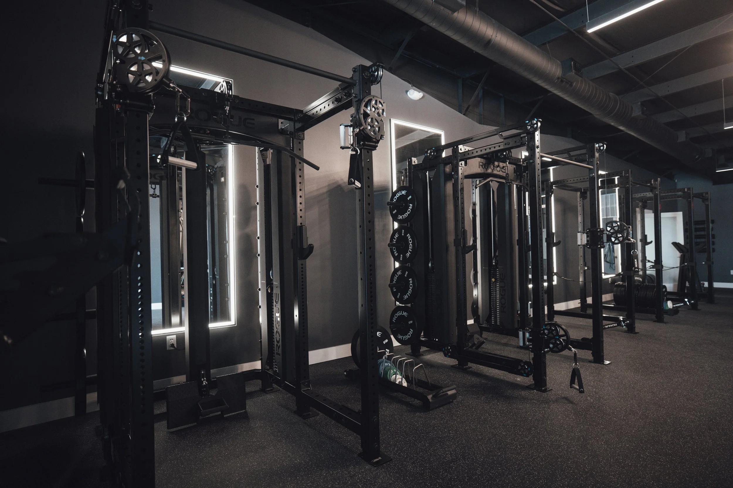 Empty modern gym with black workout equipment, mirrors, and dark flooring.
