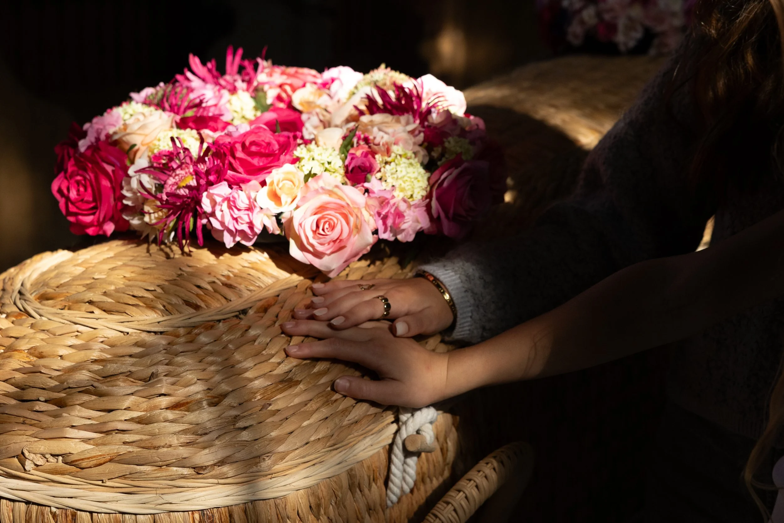 Handen op een rieten mand met bloemen tijdens een afscheidsceremonie