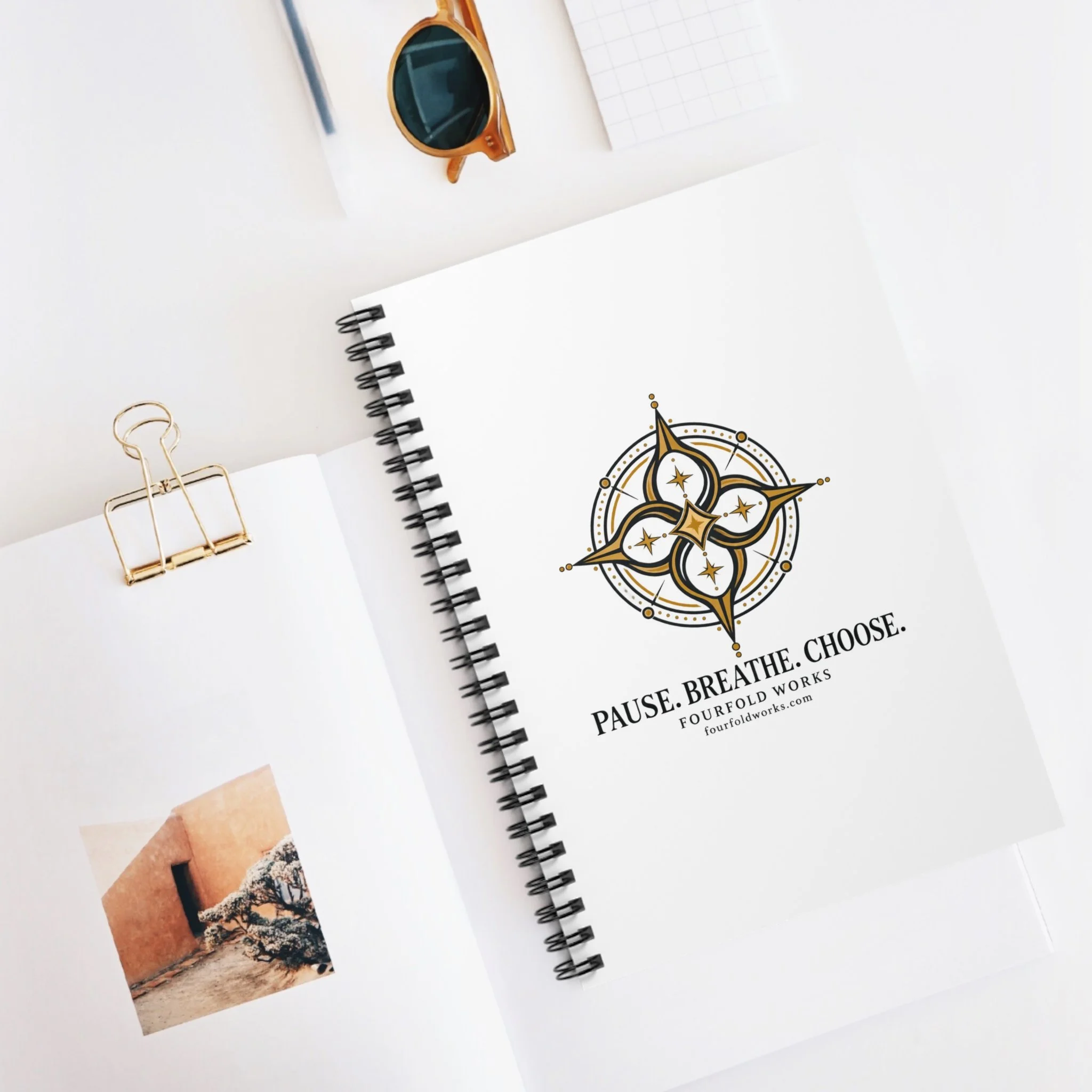 Fourfold Practice notebook on a desk beside photographs and accessories, with the compass cover visible.