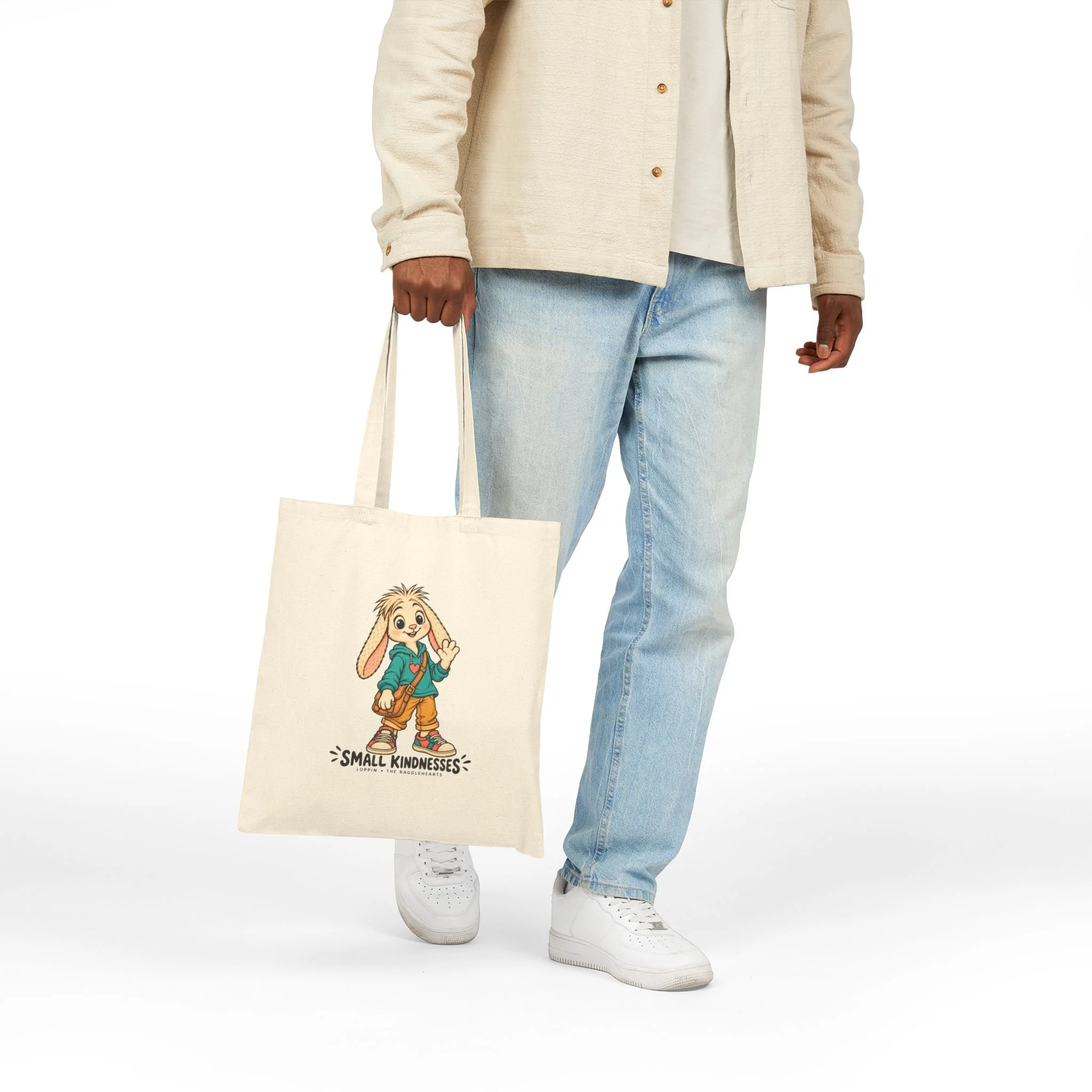 Standing model holding the Loppin Small Kindnesses canvas tote by its handles, showing the character artwork.