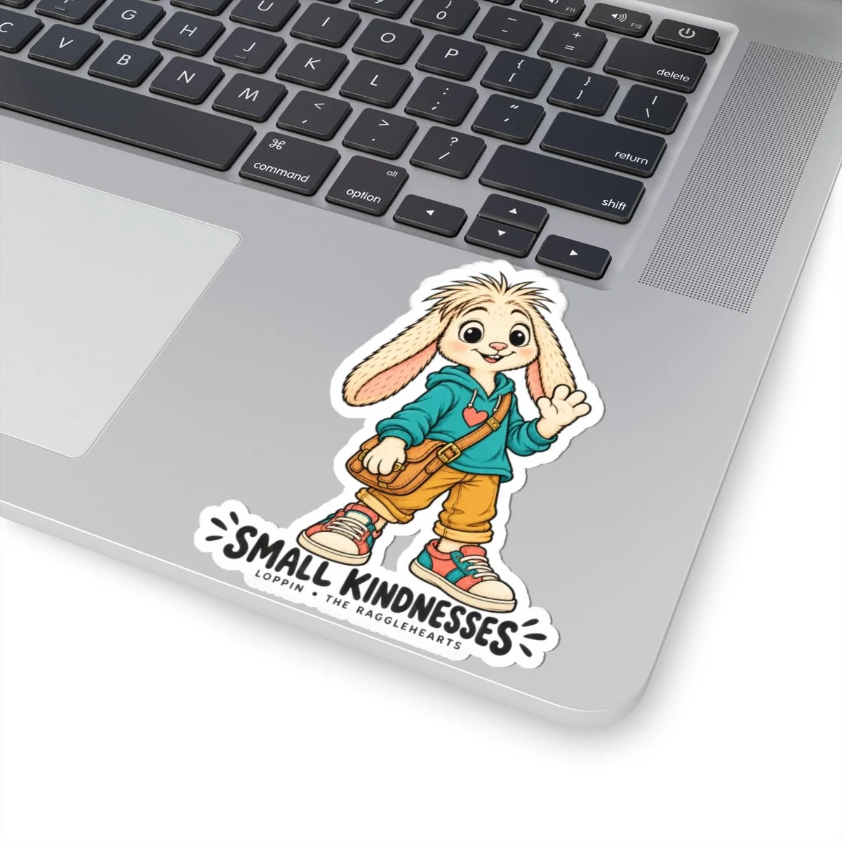 Colored Loppin Small Kindnesses Ragglehearts sticker on a laptop beside its keyboard.