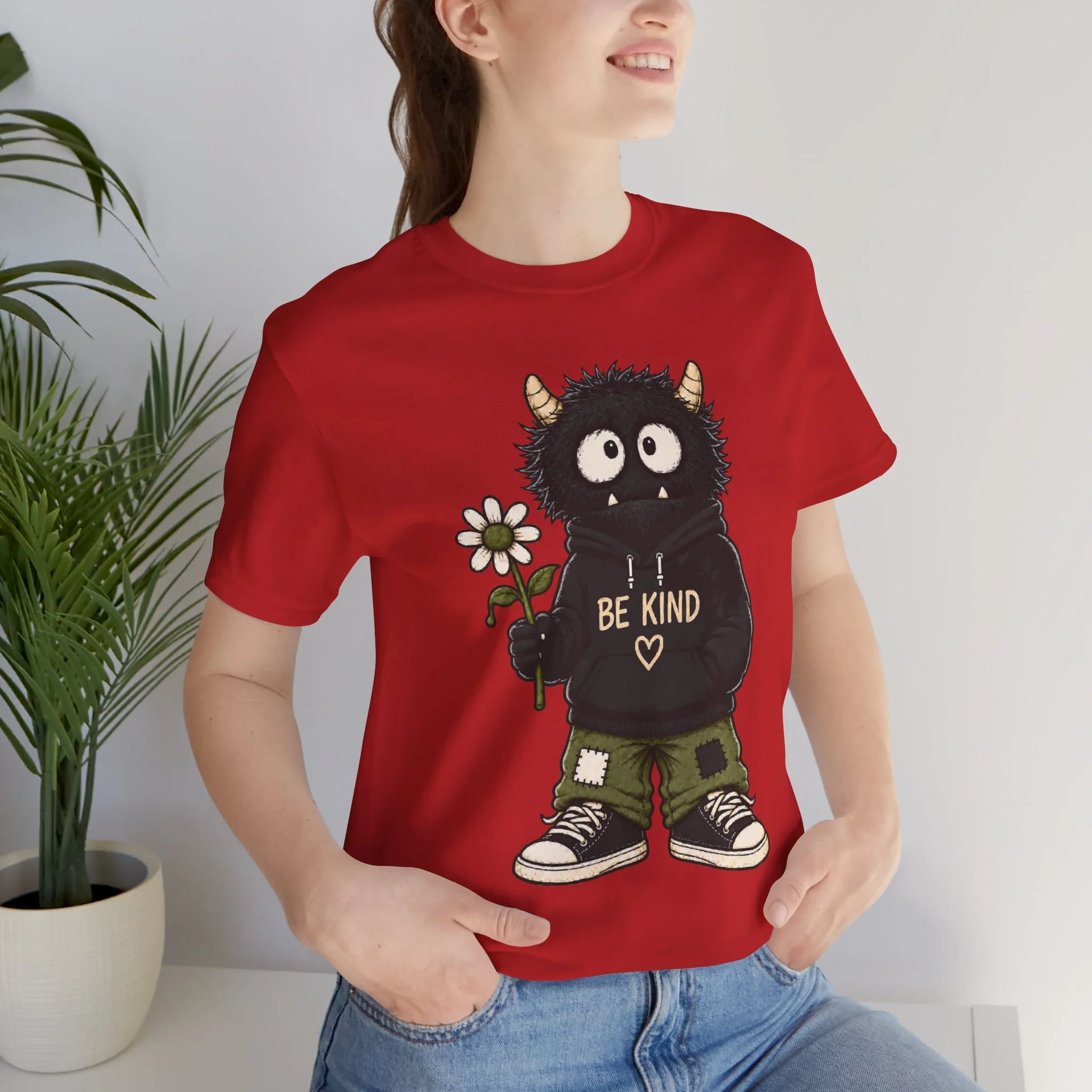 Person wearing the Red Be Kind T-shirt, showing the horned monster, daisy and BE KIND graphic.