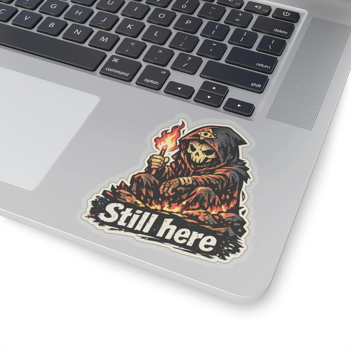 Still Here sticker on a laptop, showing the complete approved hooded reaper artwork.