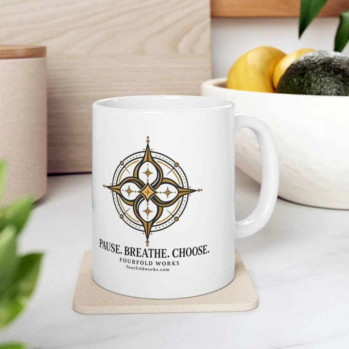 White 11 oz Pause. Breathe. Choose. compass mug on a kitchen coaster beside a fruit bowl and wooden board.