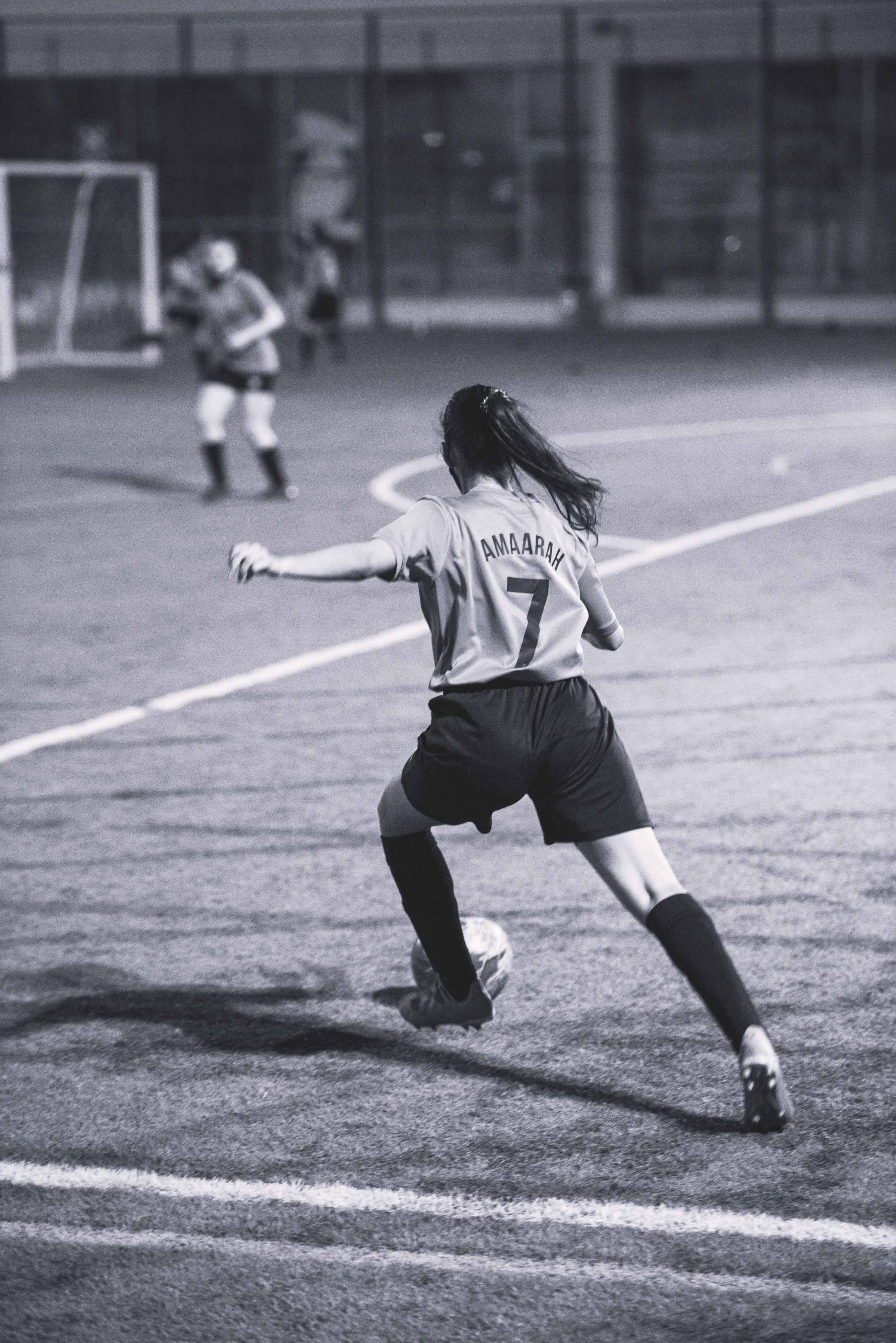 A black and white photo of a woman wearing a sports jersey, getting ready to kick a soccer ball on a field.