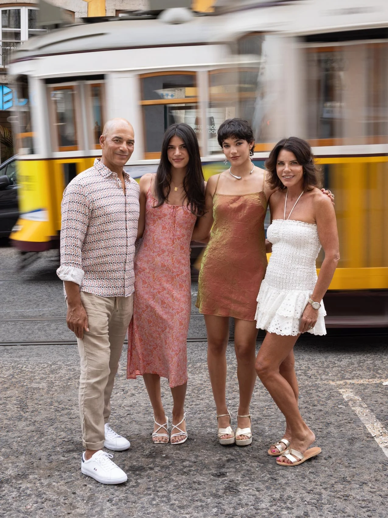 Family standing during a photoshoot  in front of a moving yellow and black streetcar, smiling and posing for the photo on a city street.