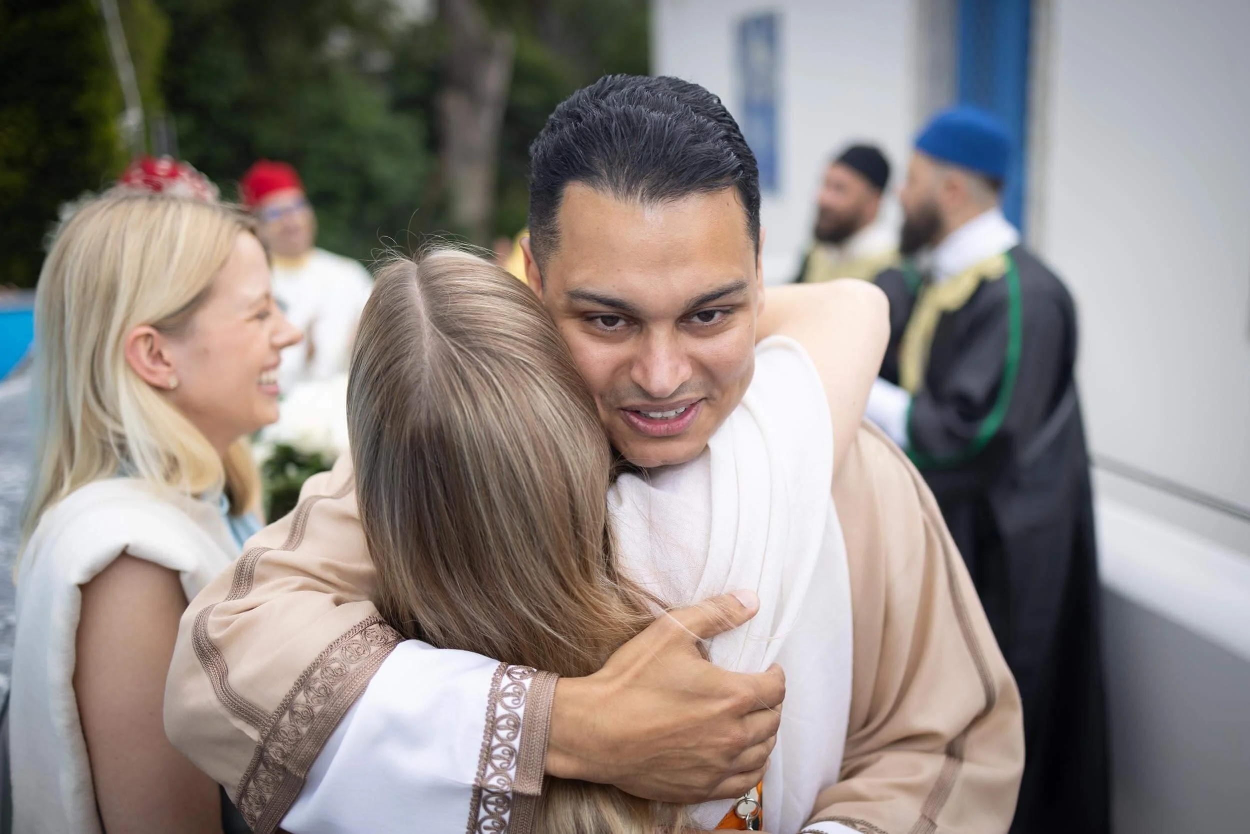 Two people hugging during a celebration, with others in the background talking and smiling.