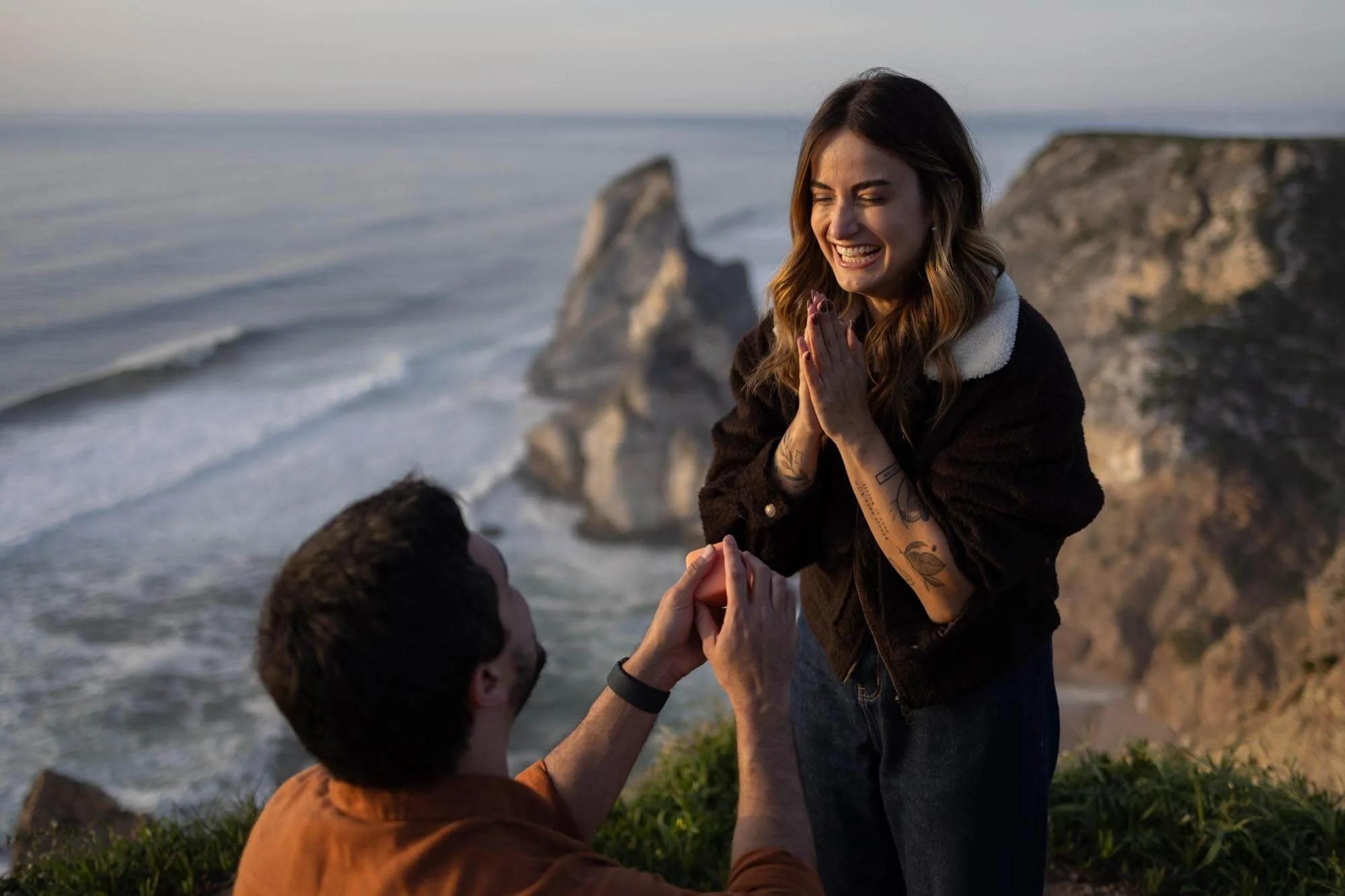 A man proposing marriage to a woman near the ocean at sunset.