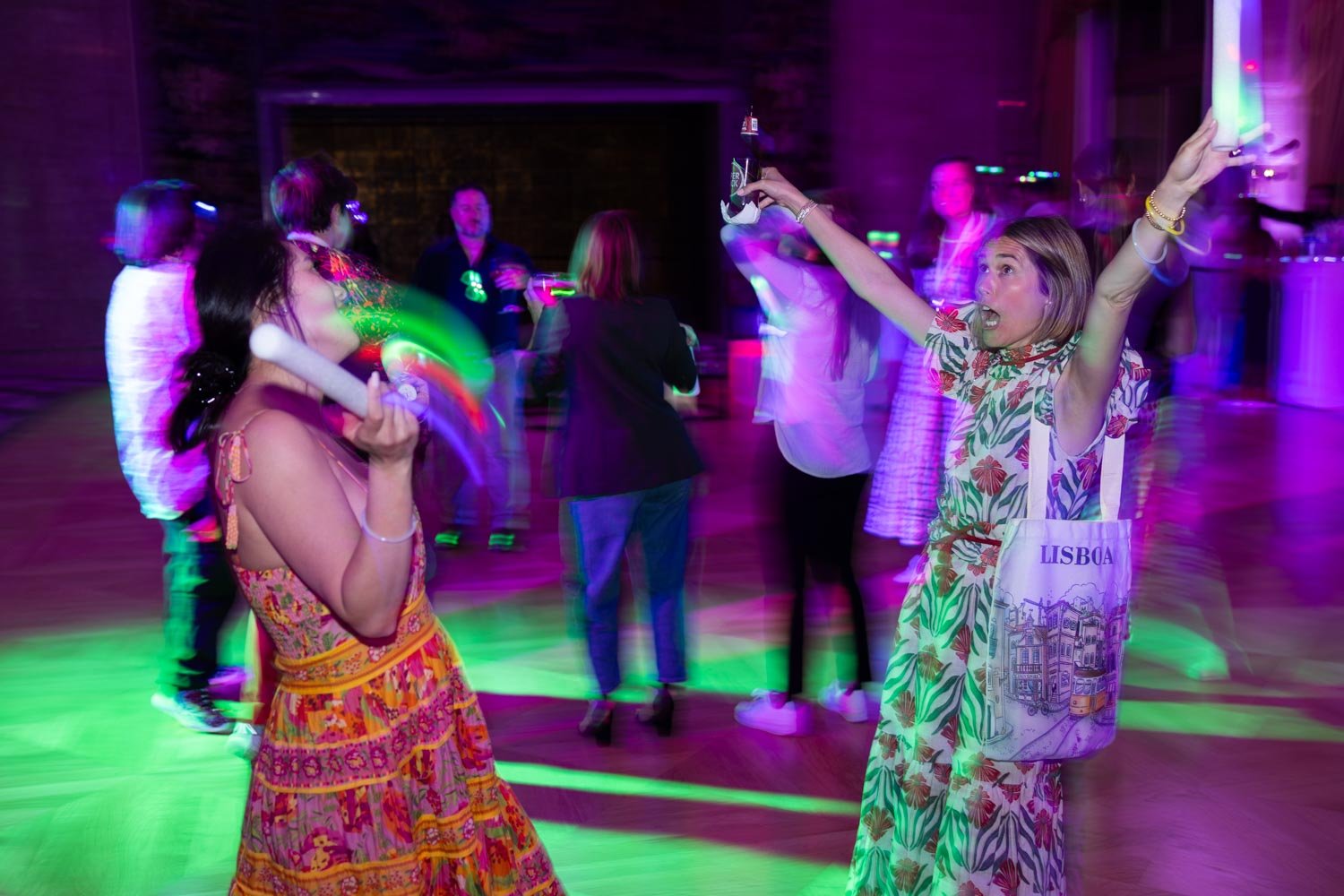People dancing and having fun at a party in Ritz hotel in Lisbon with colorful lights, some holding drinks and others with props. Girls posing for a Lisbon Photographer.