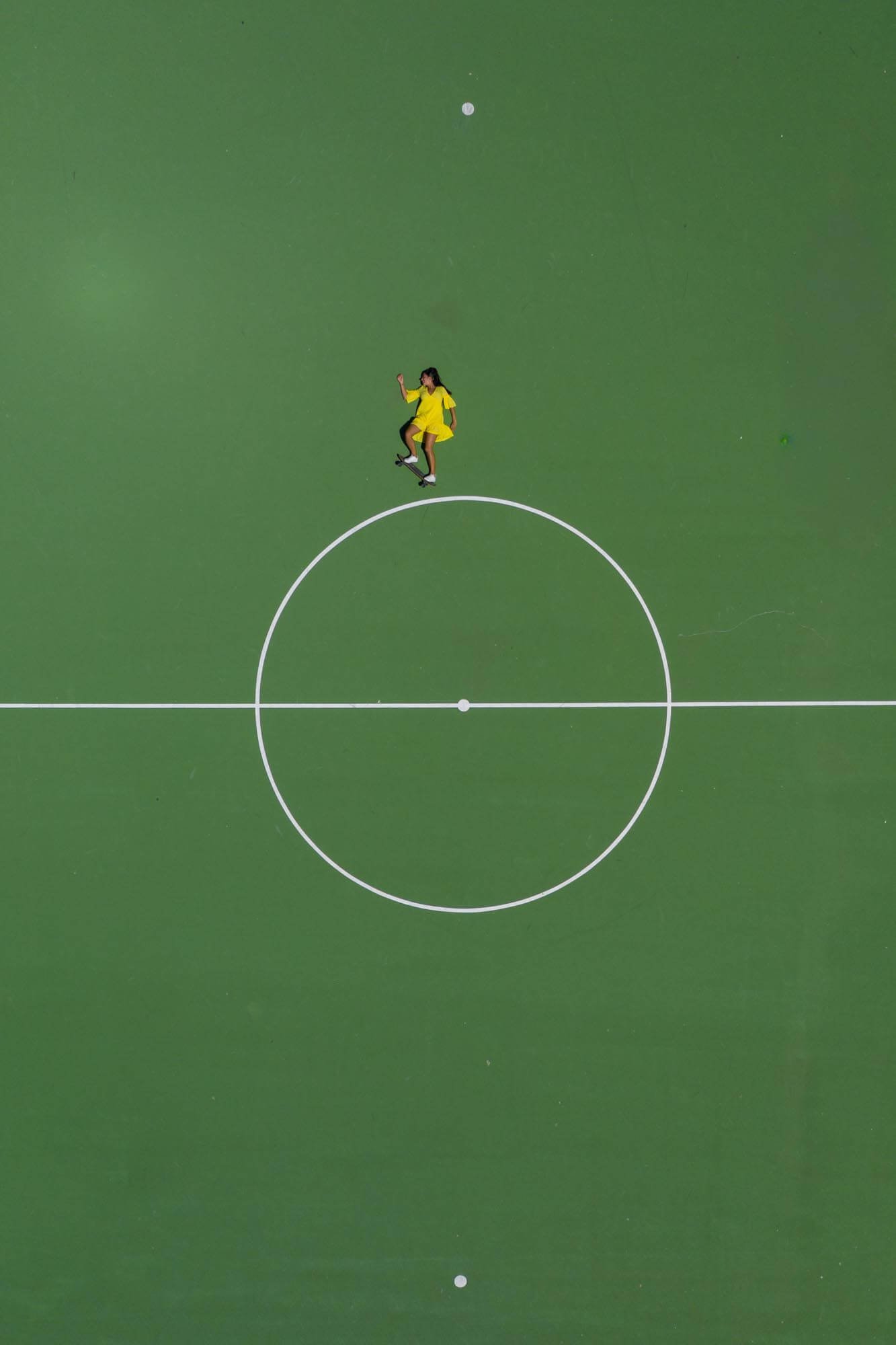 A person in a yellow outfit performs a skateboard trick on a green sports field with white lines.