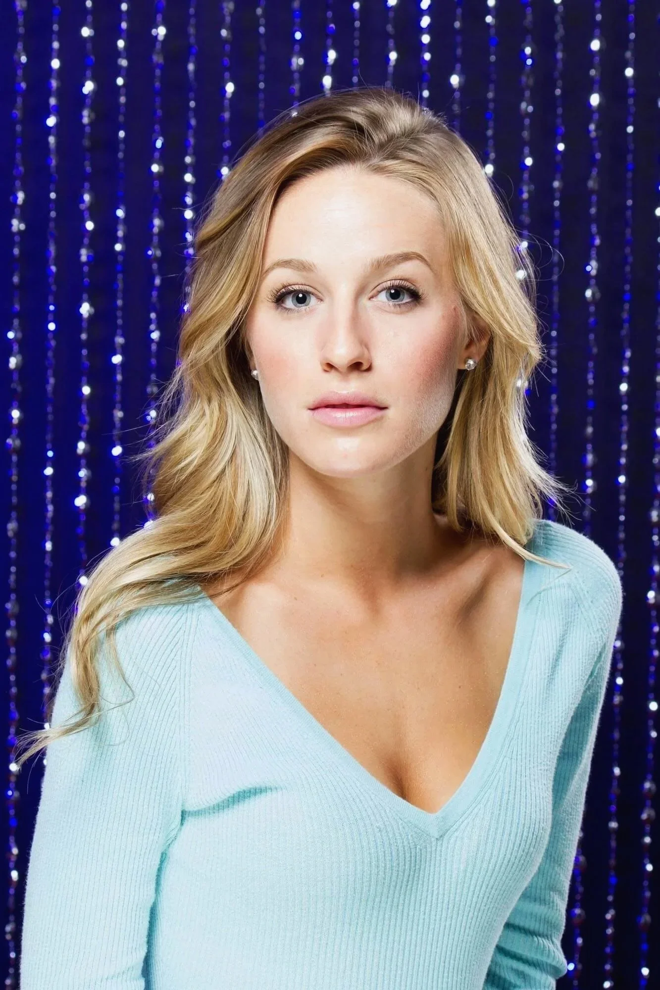 Studio Portrait session of a beautiful blond woman with a blue top an blinking background.