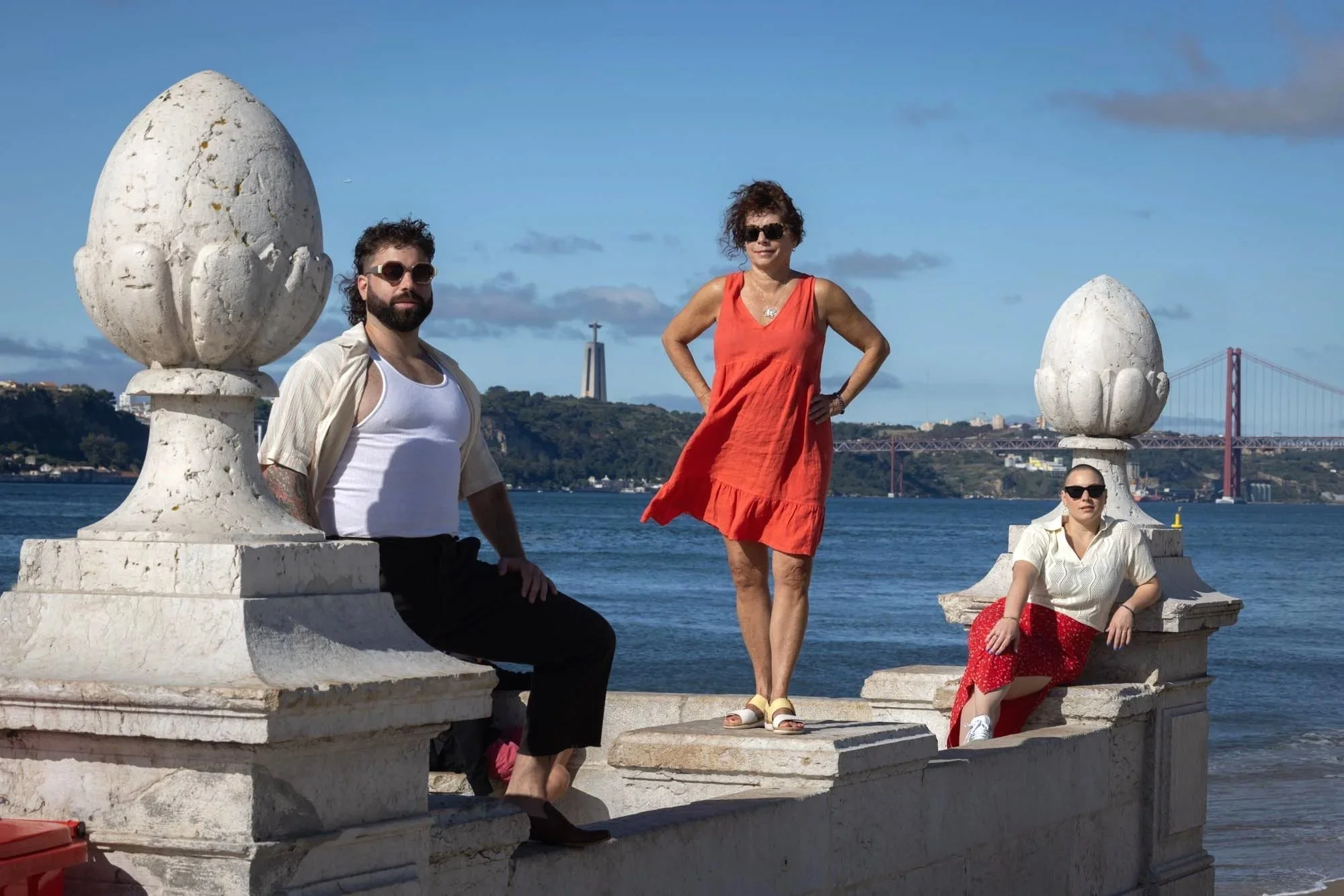 A Family  posing on a stone structure by the water, with a Lisbon bridge and the Christ  Rei statue in the background.