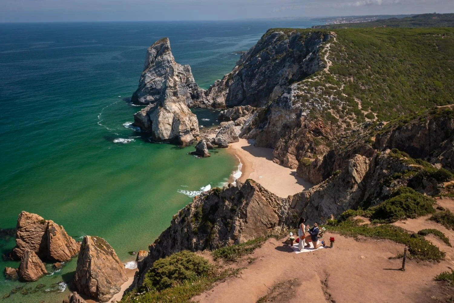 A couple getting married at a cliffside wedding ceremony overlooking a beach and rocky coastline with cliffs and green vegetation.