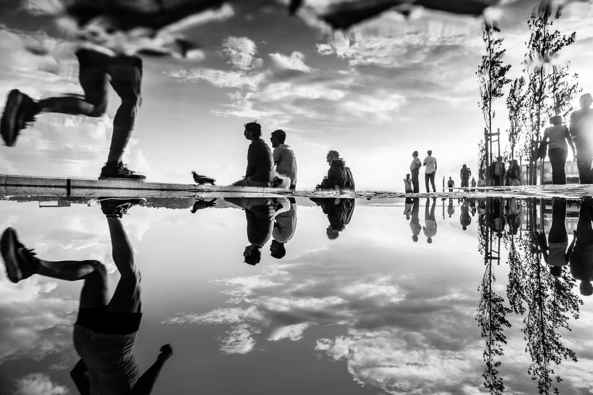 People walking and standing outdoors with reflection in a large puddle, black and white photograph