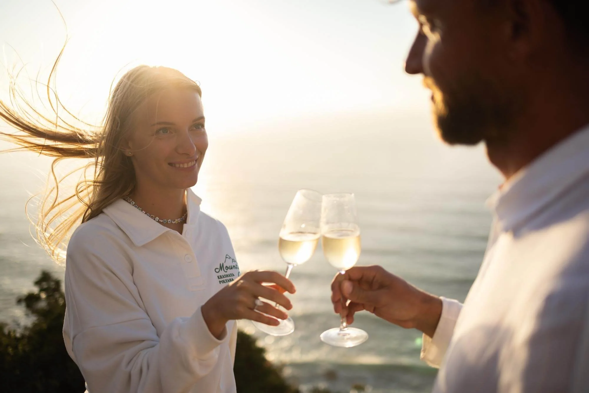 A couple drinking champagne after a sec ret proposal at Ursa Beach. Both dressed in white.