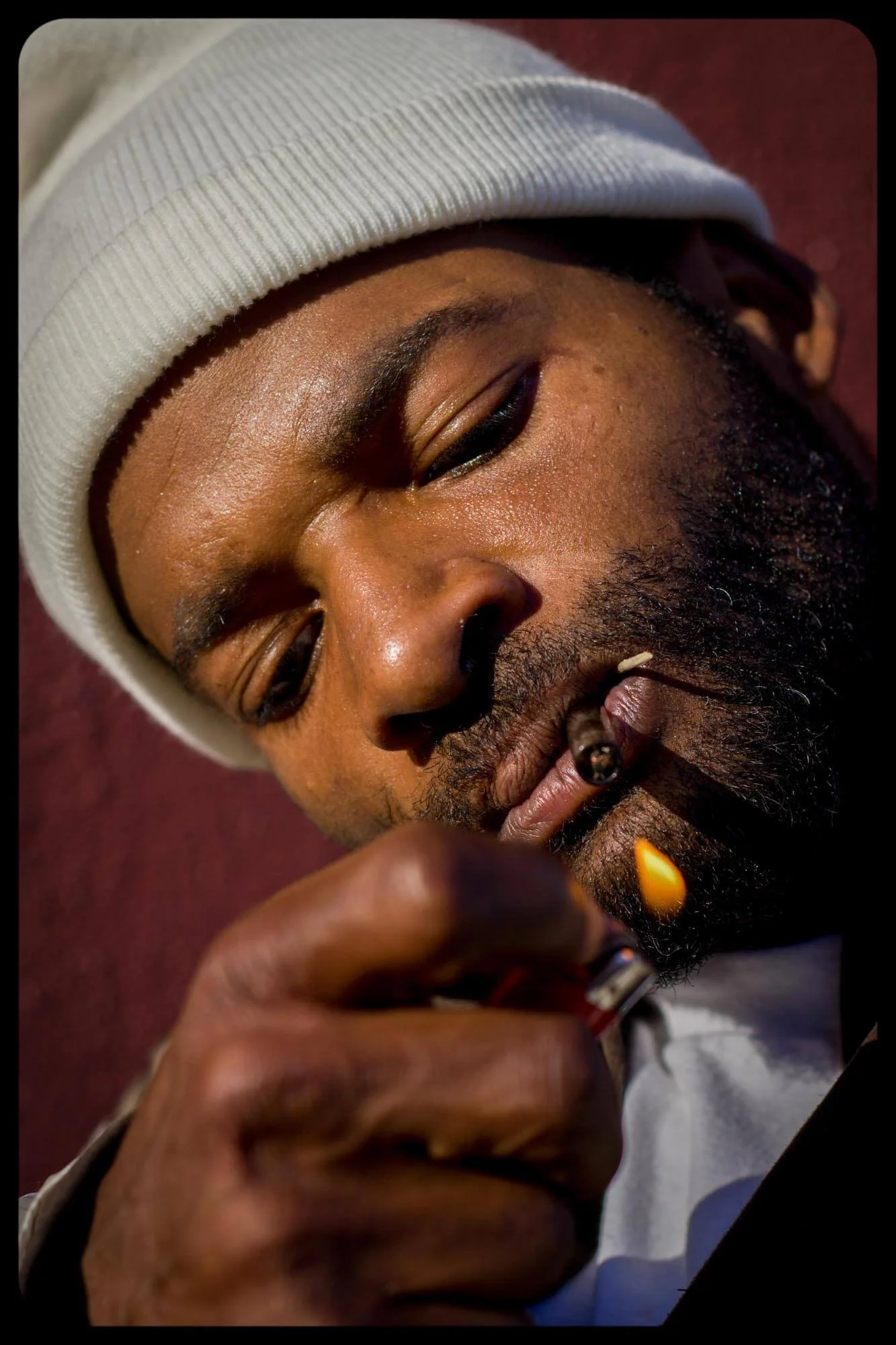 Close-up of a man with a beard and a white beanie, smoking a cigarette.