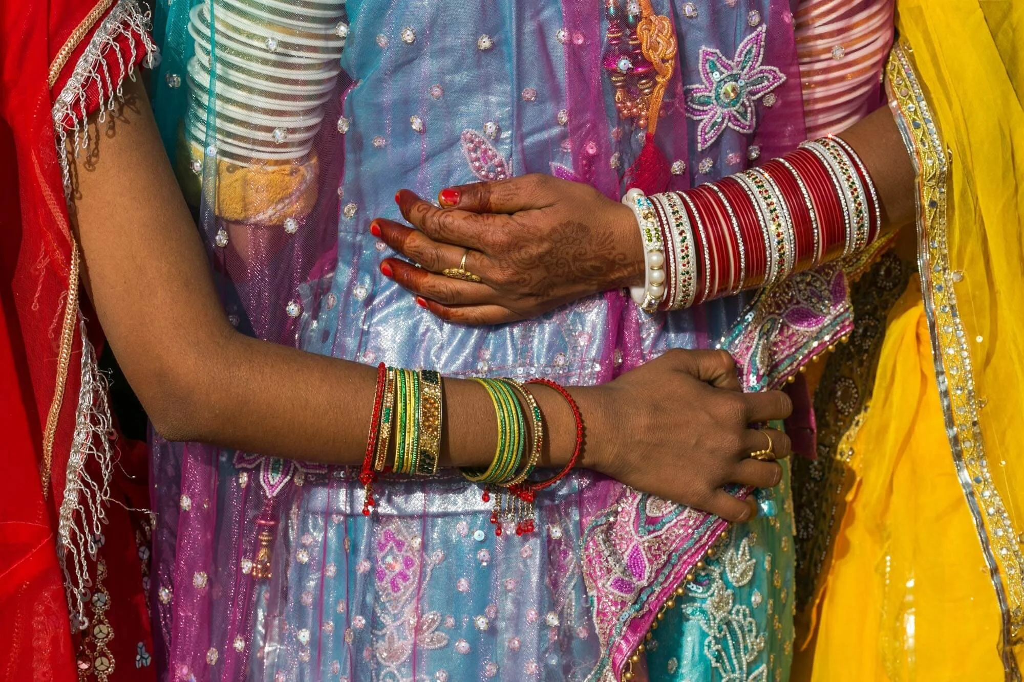 Close-up of two women wearing colorful traditional Indian attire and jewelry, with focus on their hands and bangles.