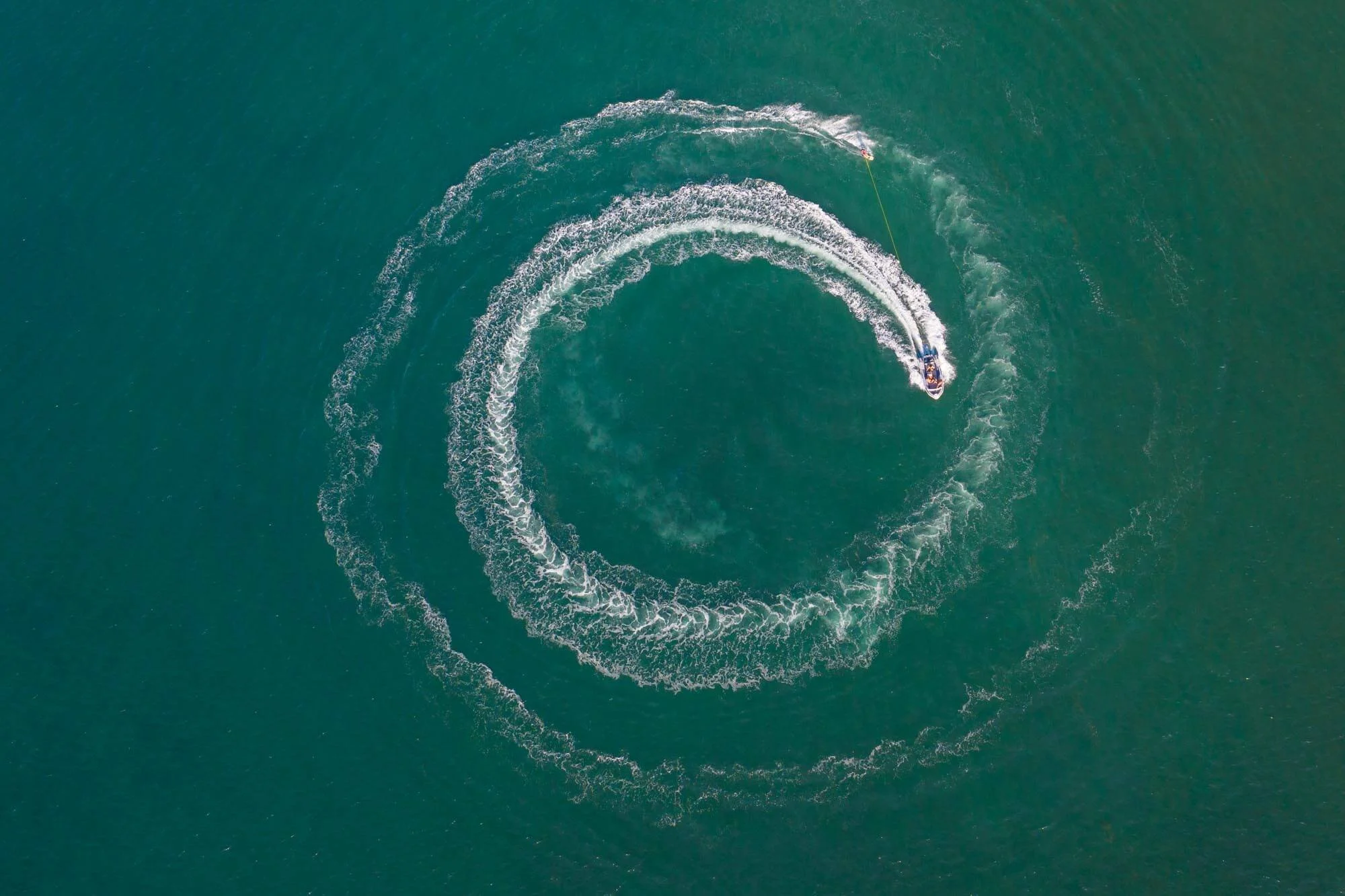 An aerial view of a speedboat creating a large circular wake pattern in the water.