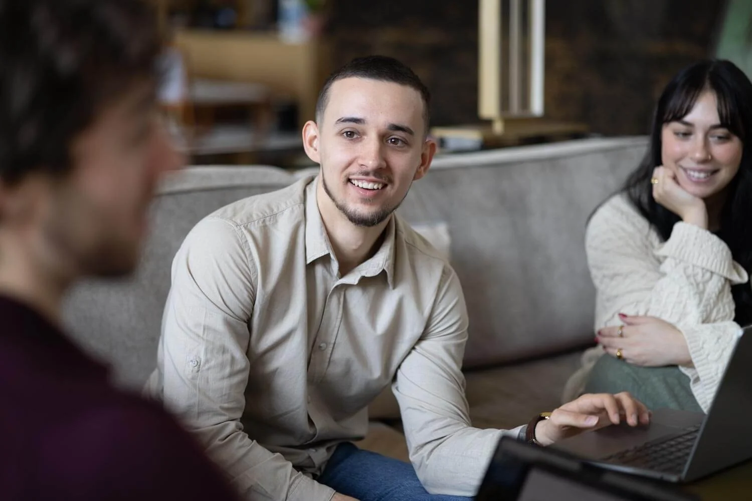 Three people sitting on a couch, engaging in a conversation, with a laptop in front of them.