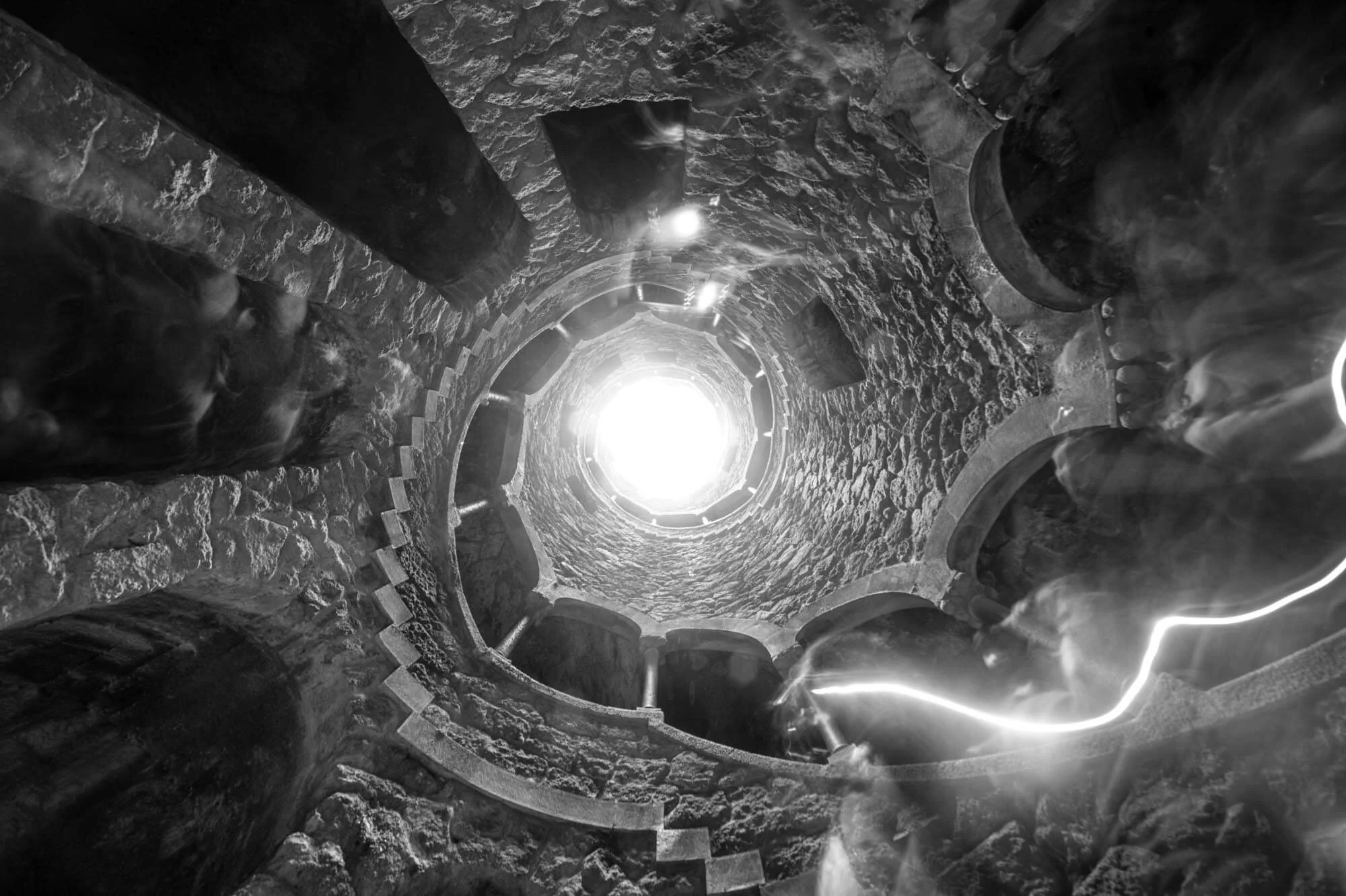 Looking up inside a stone spiral staircase with bright light at the top opening.