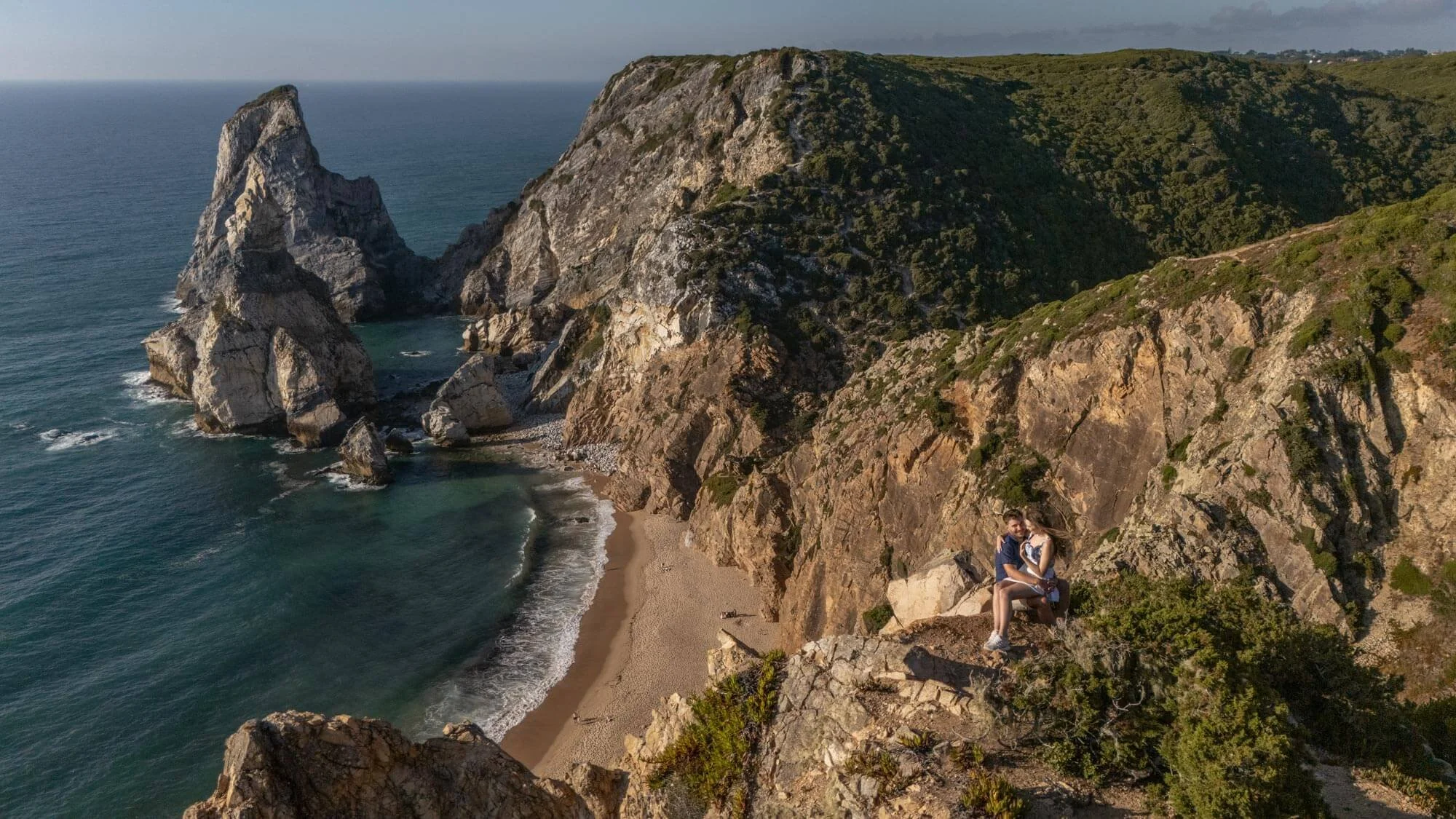 A drone photo of a couple at the top of Ursa Beach cliff, during a secret proposal photoshoot.
