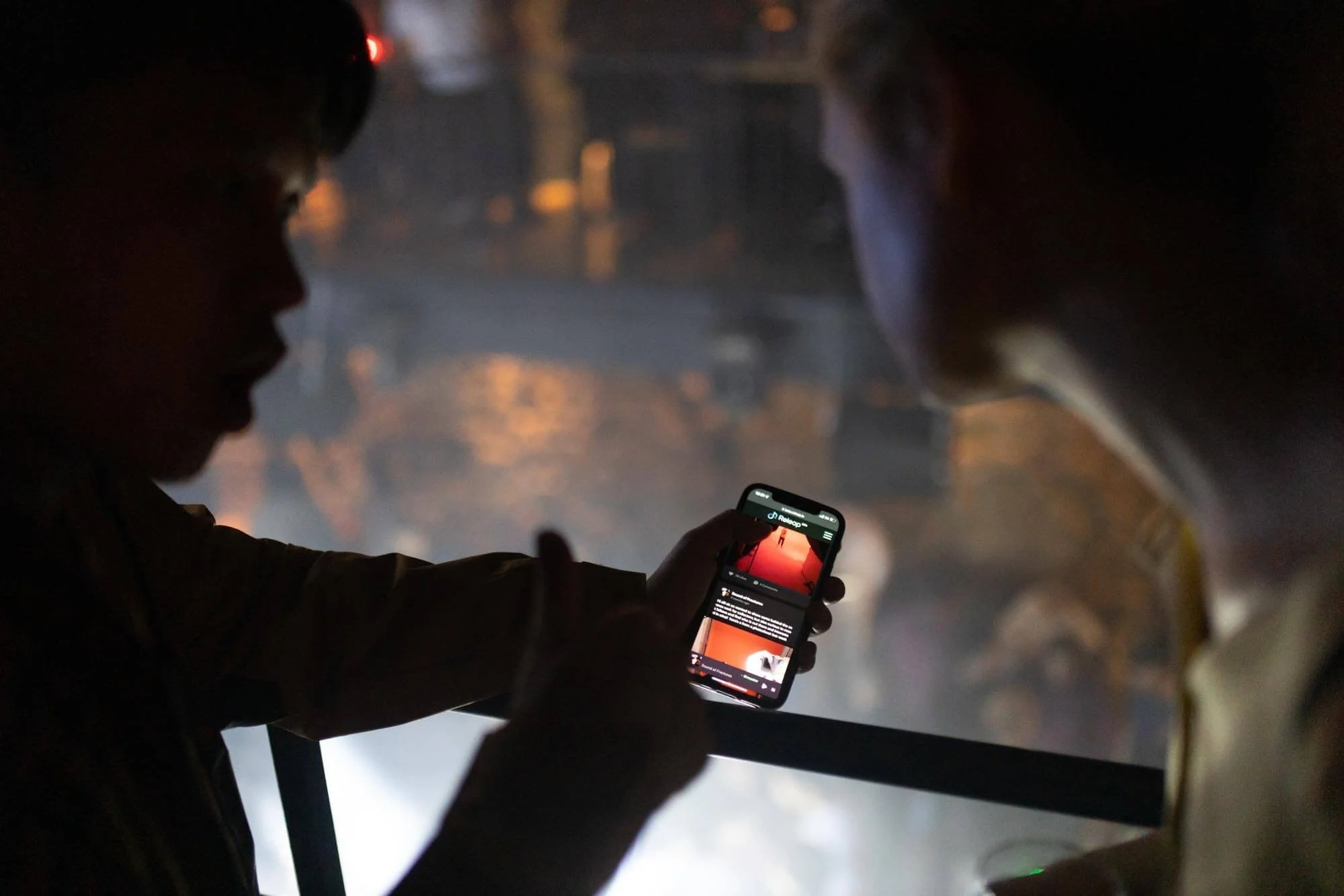 Two children sitting in a vehicle, one holding a smartphone showing a social media post, with the background blurred and dark.
