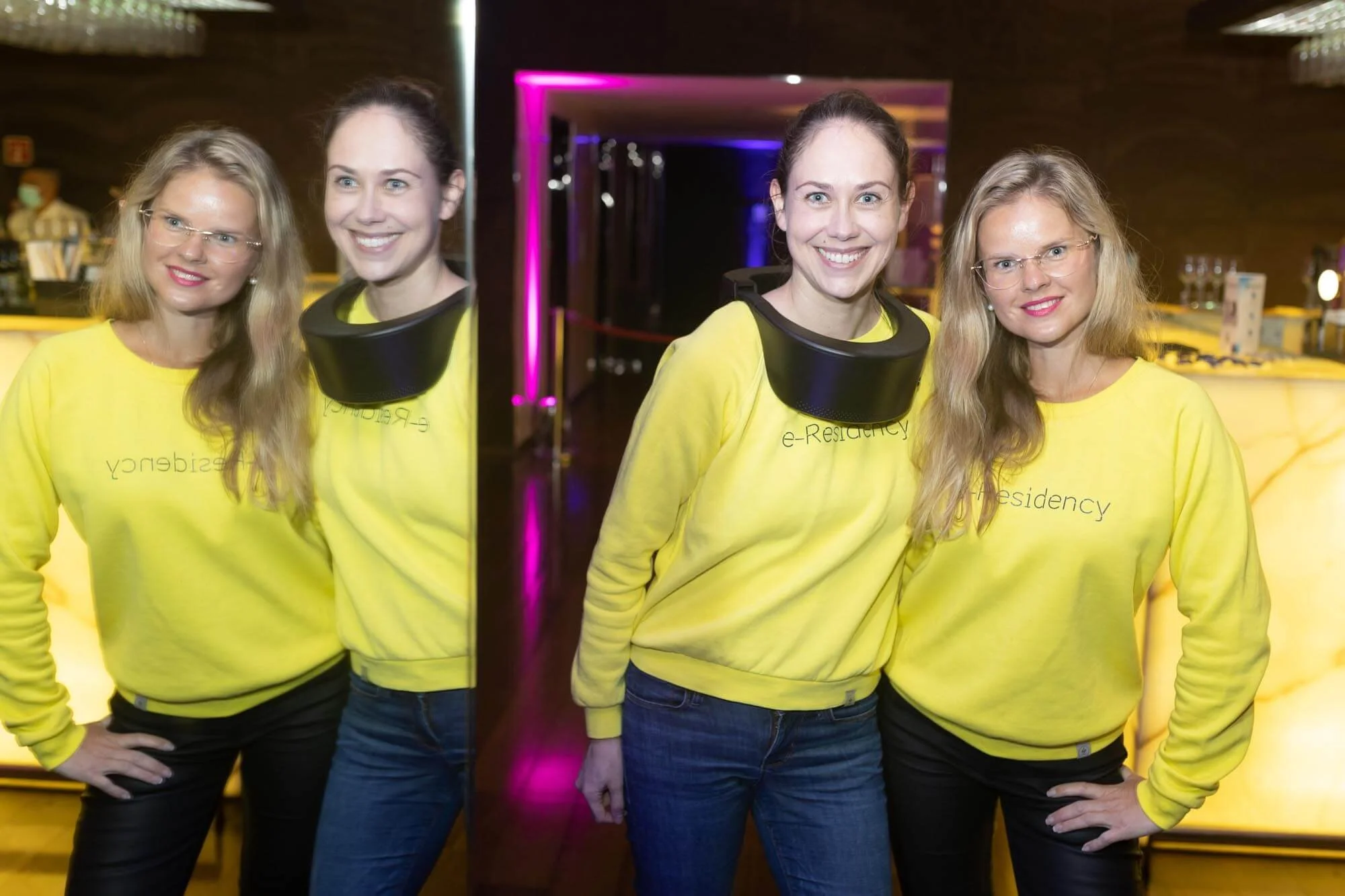 Four women wearing yellow sweatshirts with 'e-Residency' printed on them, standing in front of a mirrored wall, smiling, with a bar and colorful lighting in the background.