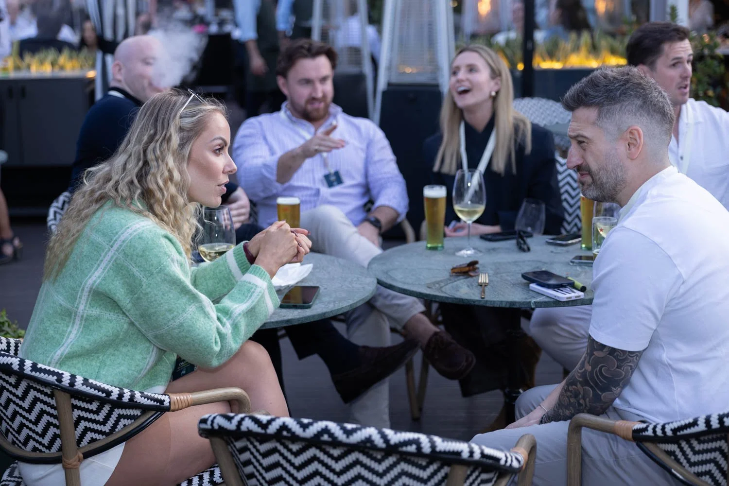 Group of people sitting around a table at a social gathering, outdoors, with drinks and snacks, engaging in conversation and laughter. Photo captured by a Lisbon Event Photographer.