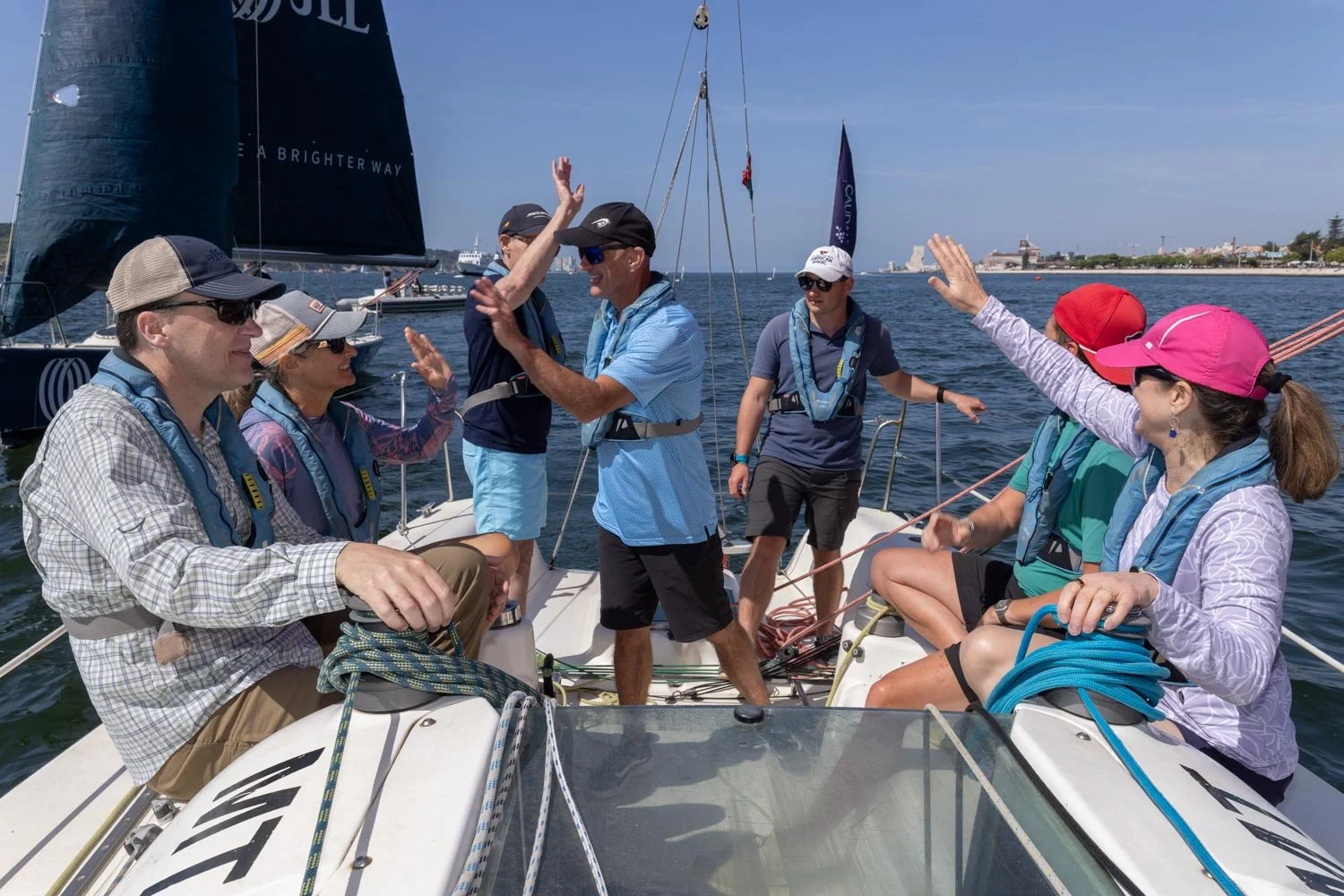 Group of people on a sailboat celebrating and high-fiving each other on a sunny day at the water.