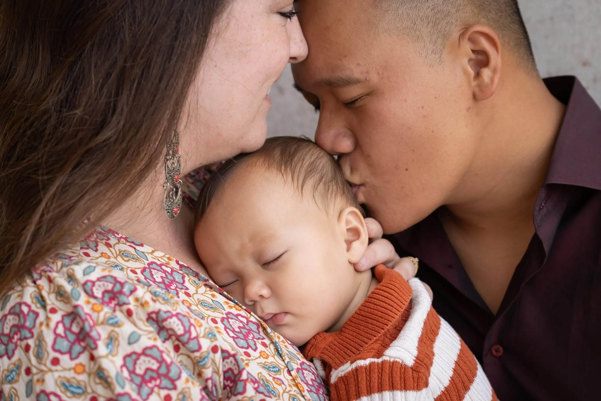 Lovely Family Photoshoot, father kissing a baby resting on the chest of the mother.