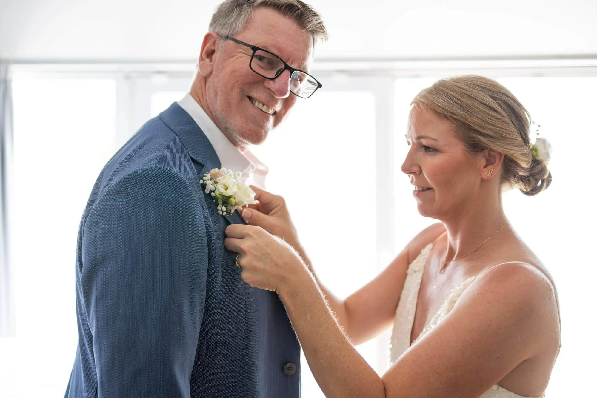A bride pinning a boutonniere on a groom during their wedding.
