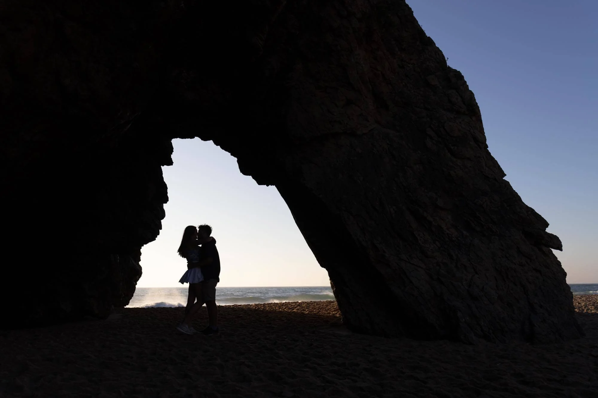 Silhouette of couple kissing under the rock on the Sintra coastline during the engagement photoshoot.